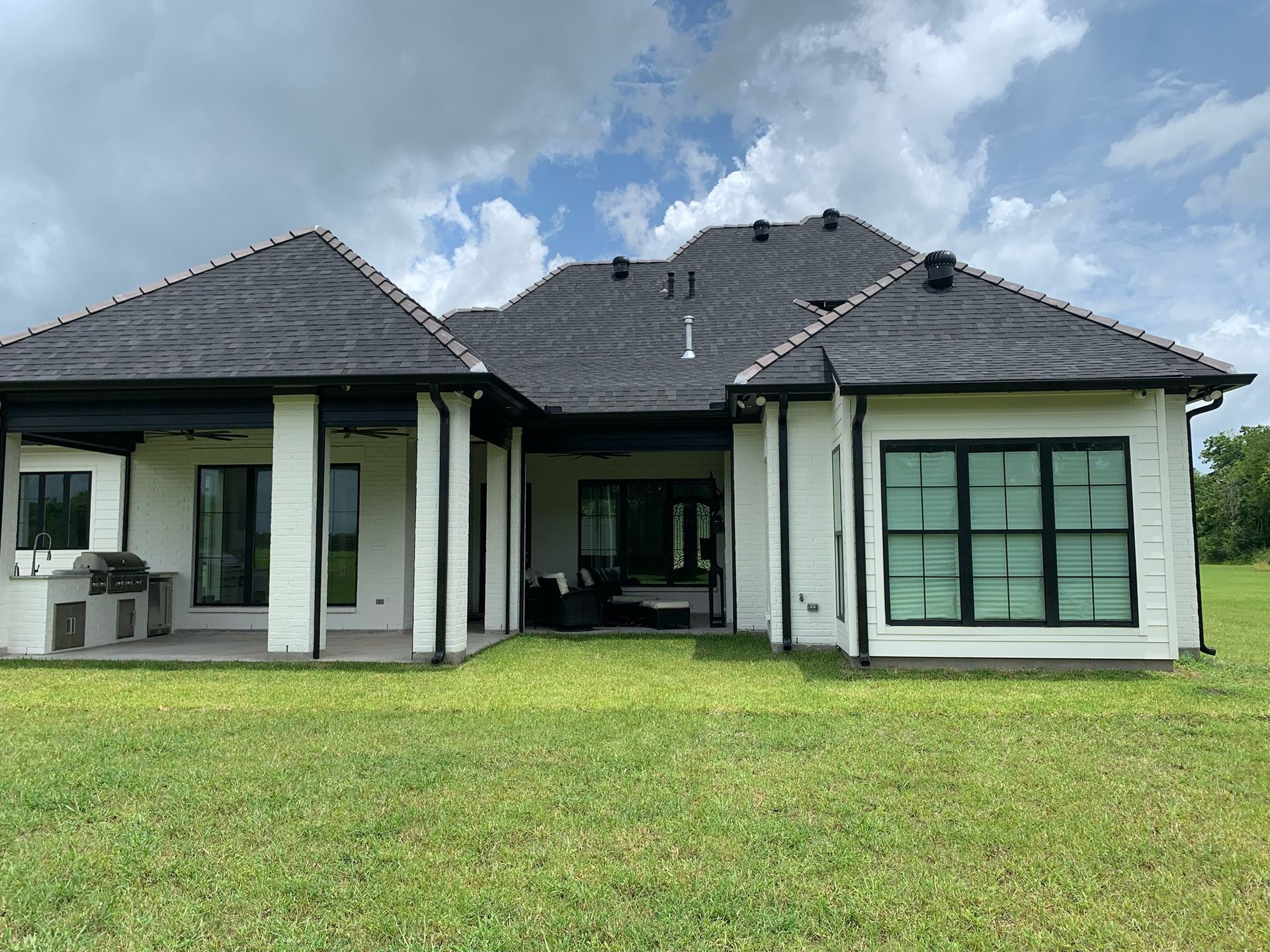 Modern single-story house with dark roof, white walls, and large lawn in front
