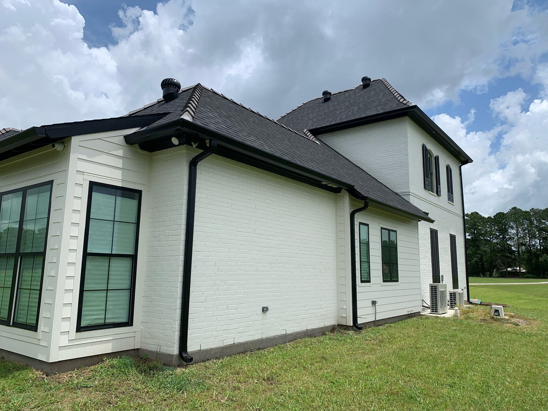 Modern white two-story house with dark roof and large windows on a grassy lot under a cloudy sky
