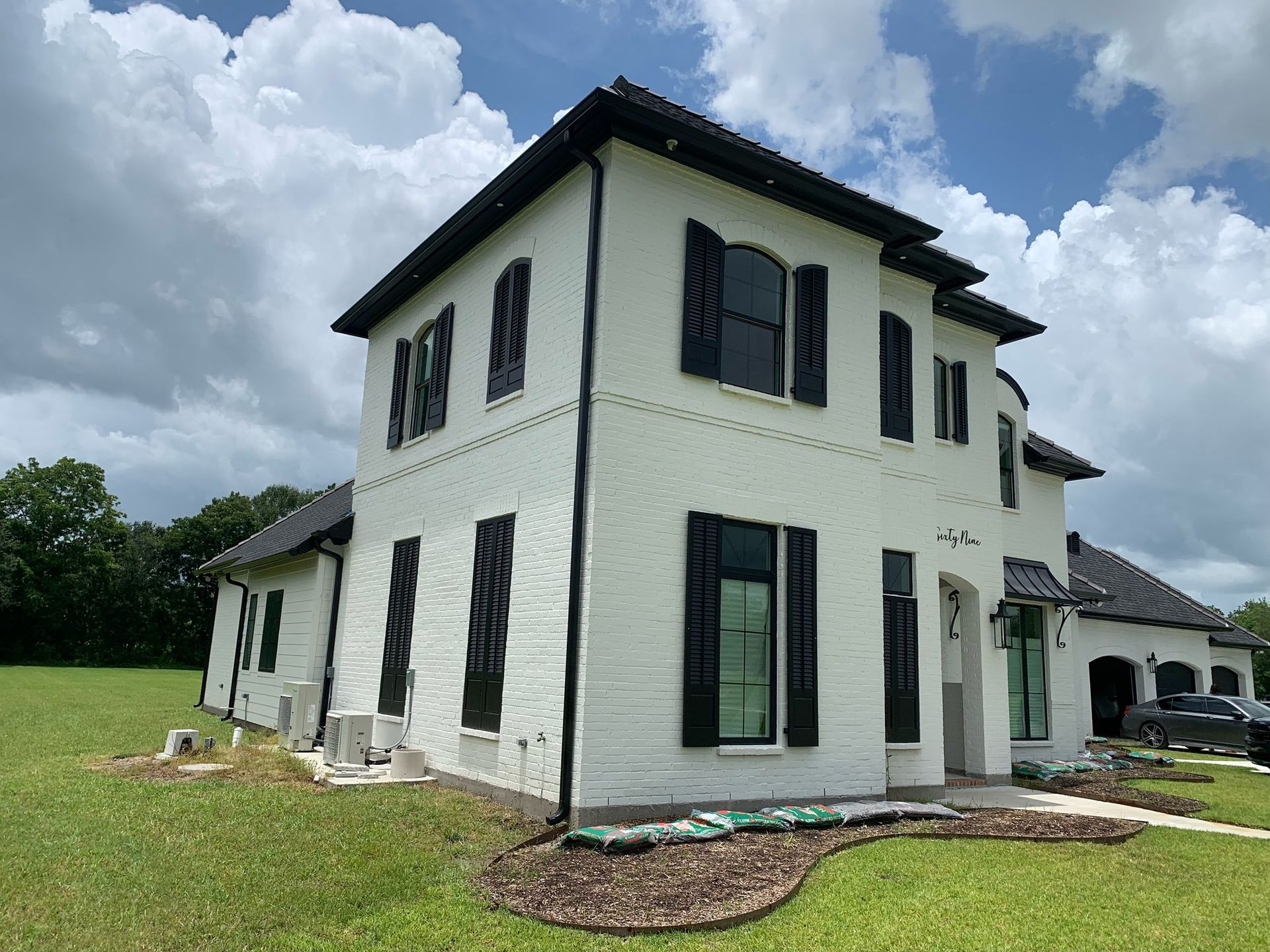 New two-story white house with black shutters and a dark roof on a grassy lot under cloudy sky