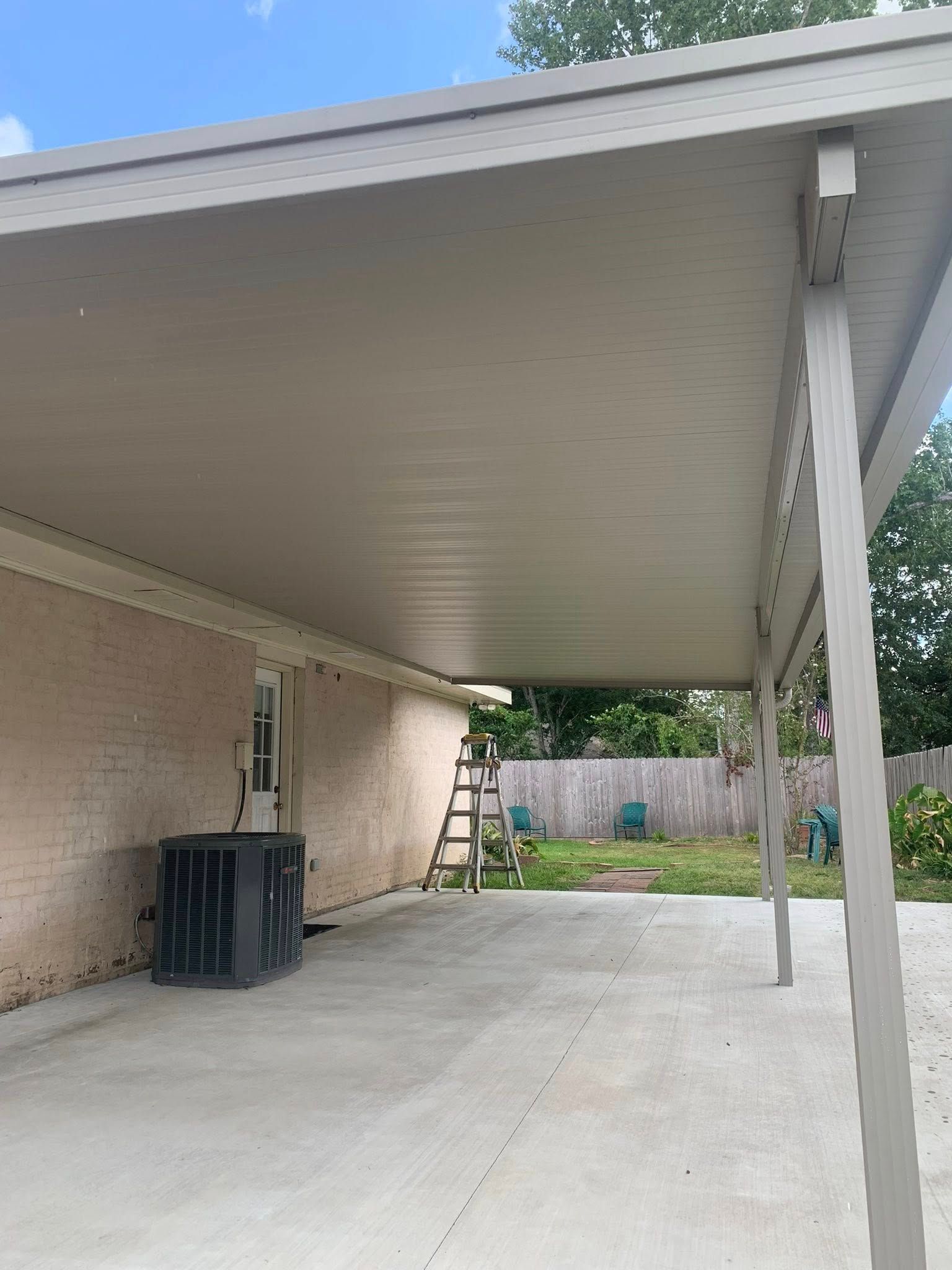 Covered patio beside a brick house, with a concrete slab, ladder, and outdoor AC unit