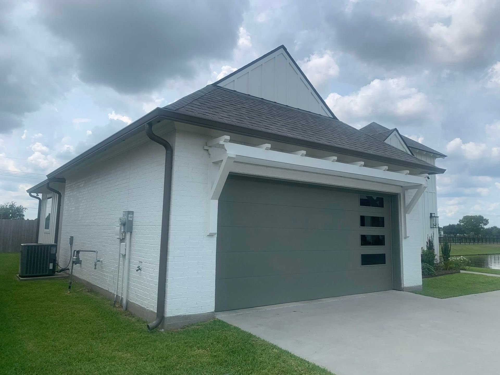 Modern white house exterior with a gray garage door, driveway, and cloudy sky