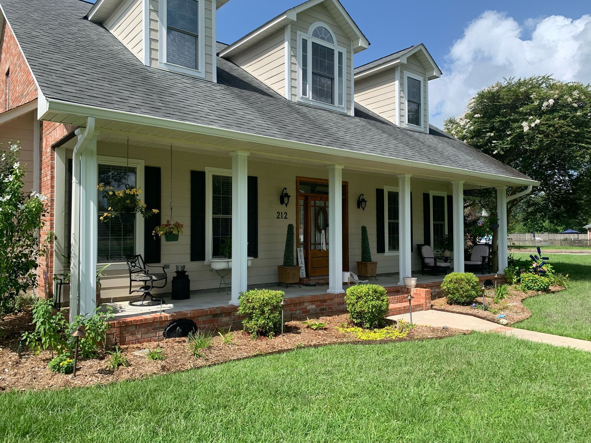 Front porch of a white house with columns, dormer windows, and a green lawn under a sunny sky