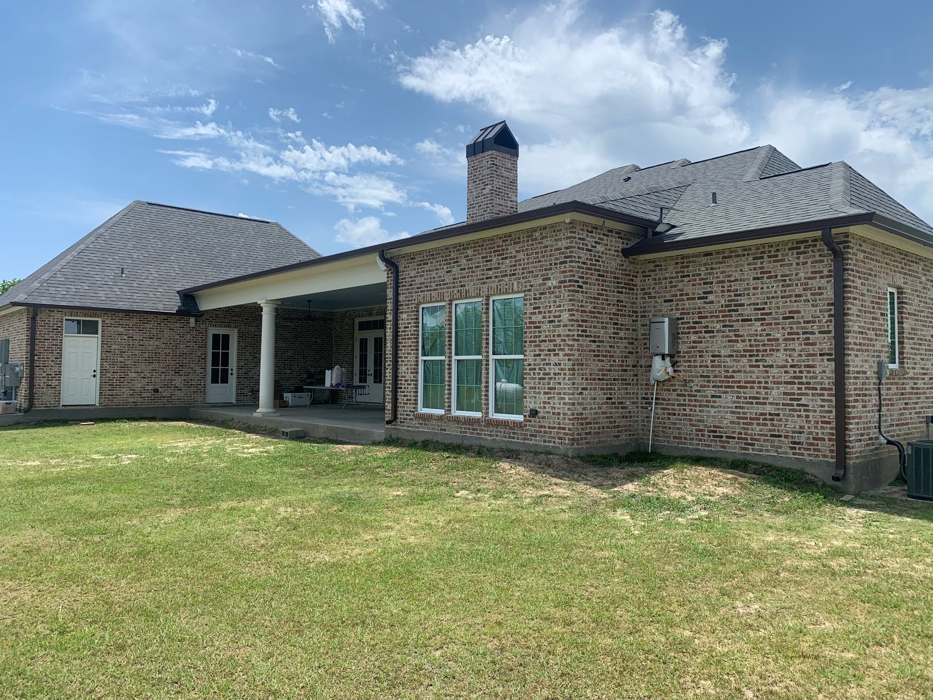 Brick house with a covered patio, chimney, and large grassy backyard under a blue sky