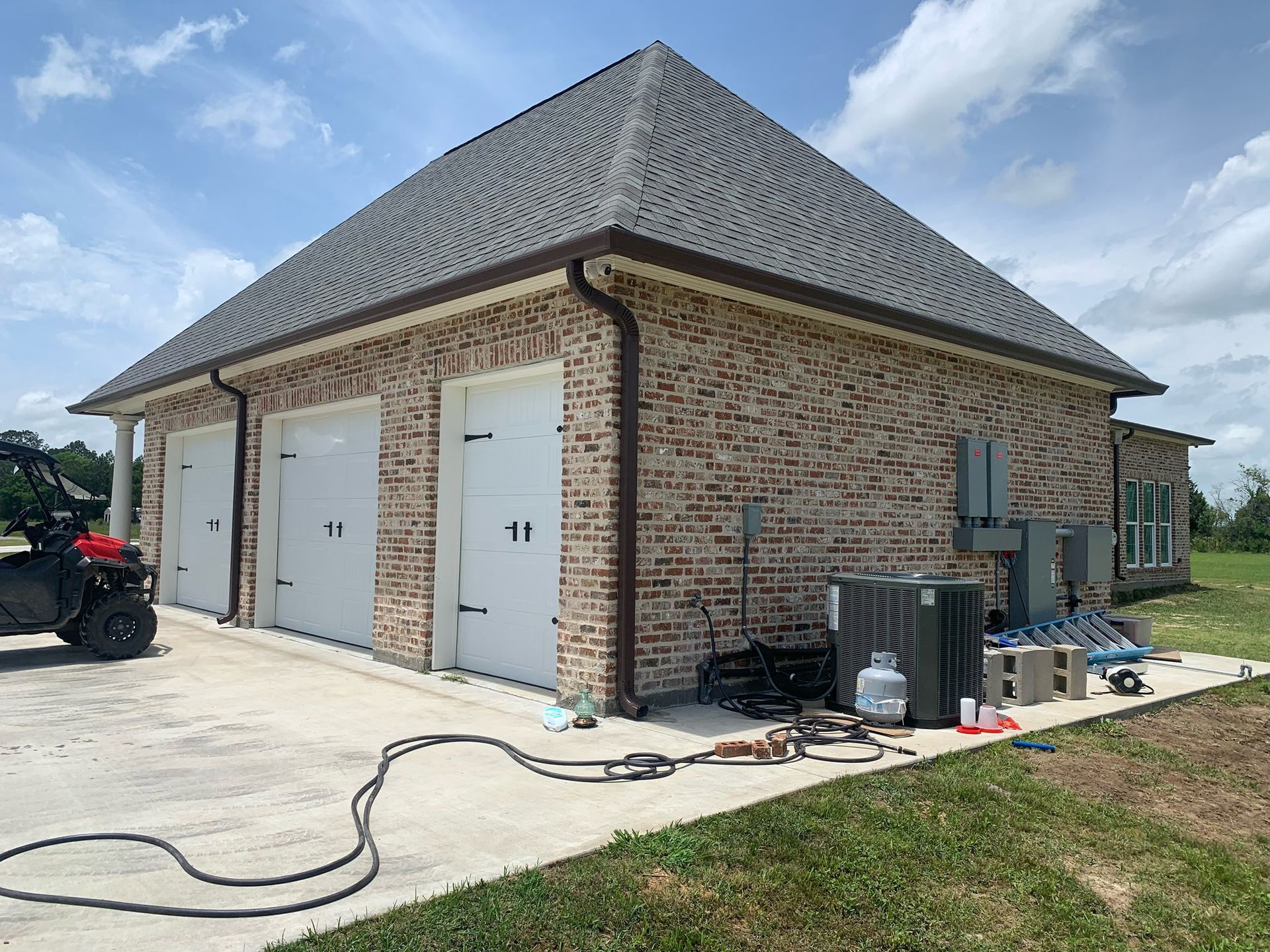Brick garage with two white doors, a gray shingled roof, and landscaping work in progress outside.