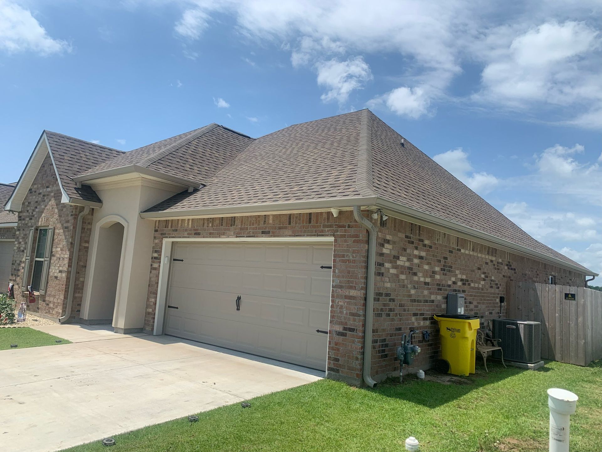 Brick suburban house with two-car garage, beige roof, driveway, and green lawn under a blue sky