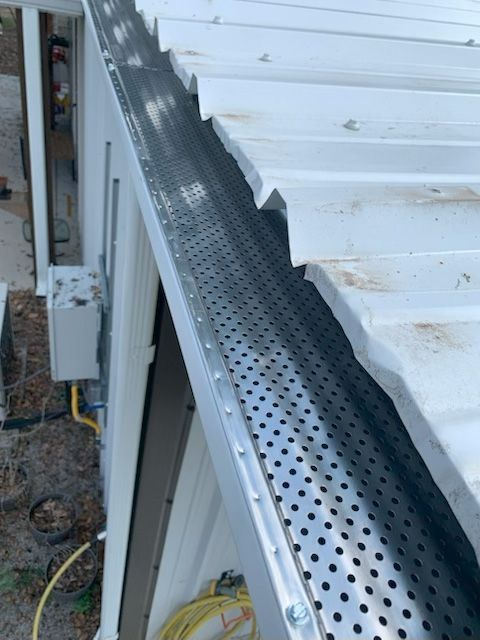 Perforated metal gutter along a white roof edge above an exterior wall