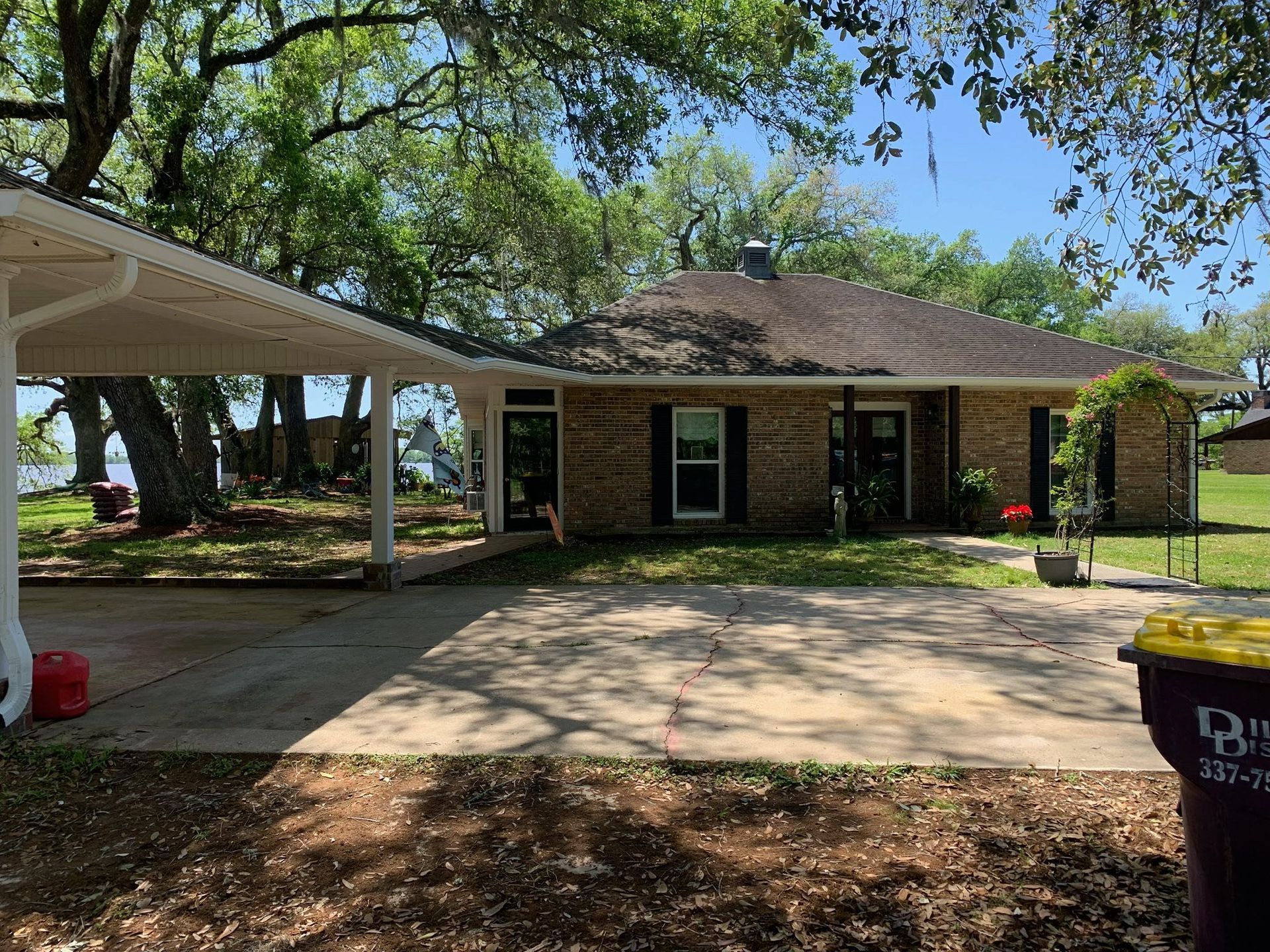Single-story brick house with carport, driveway, and large trees in the yard