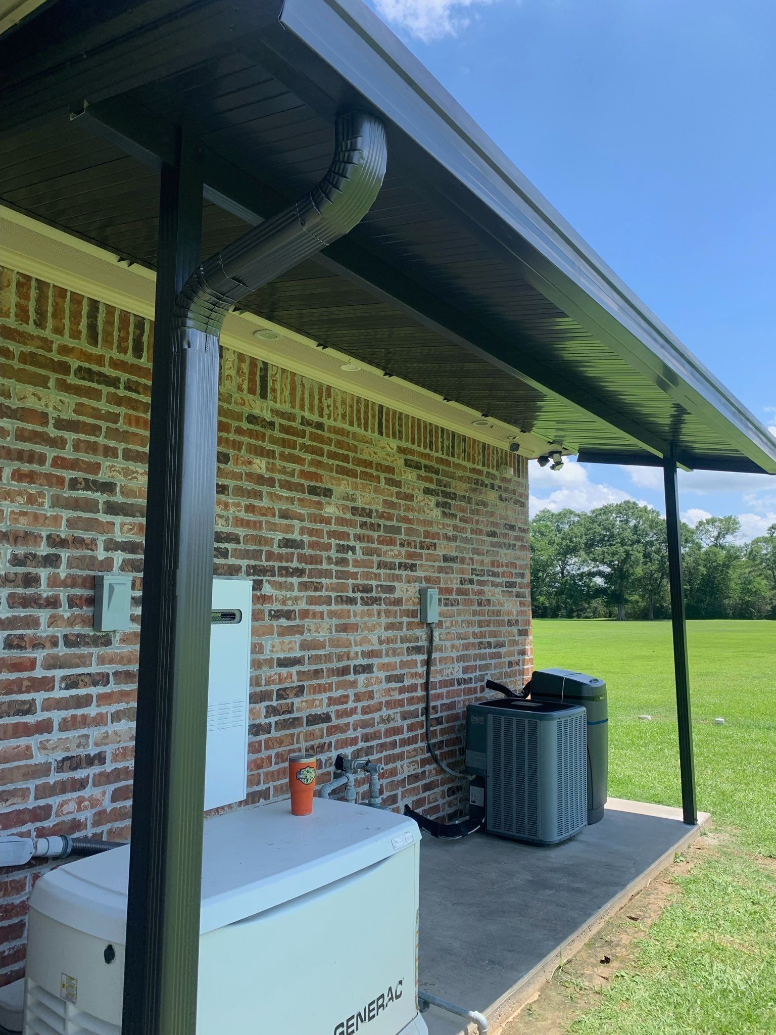 Brick house side porch with metal awning, white generator, and air conditioner beside a grassy field.
