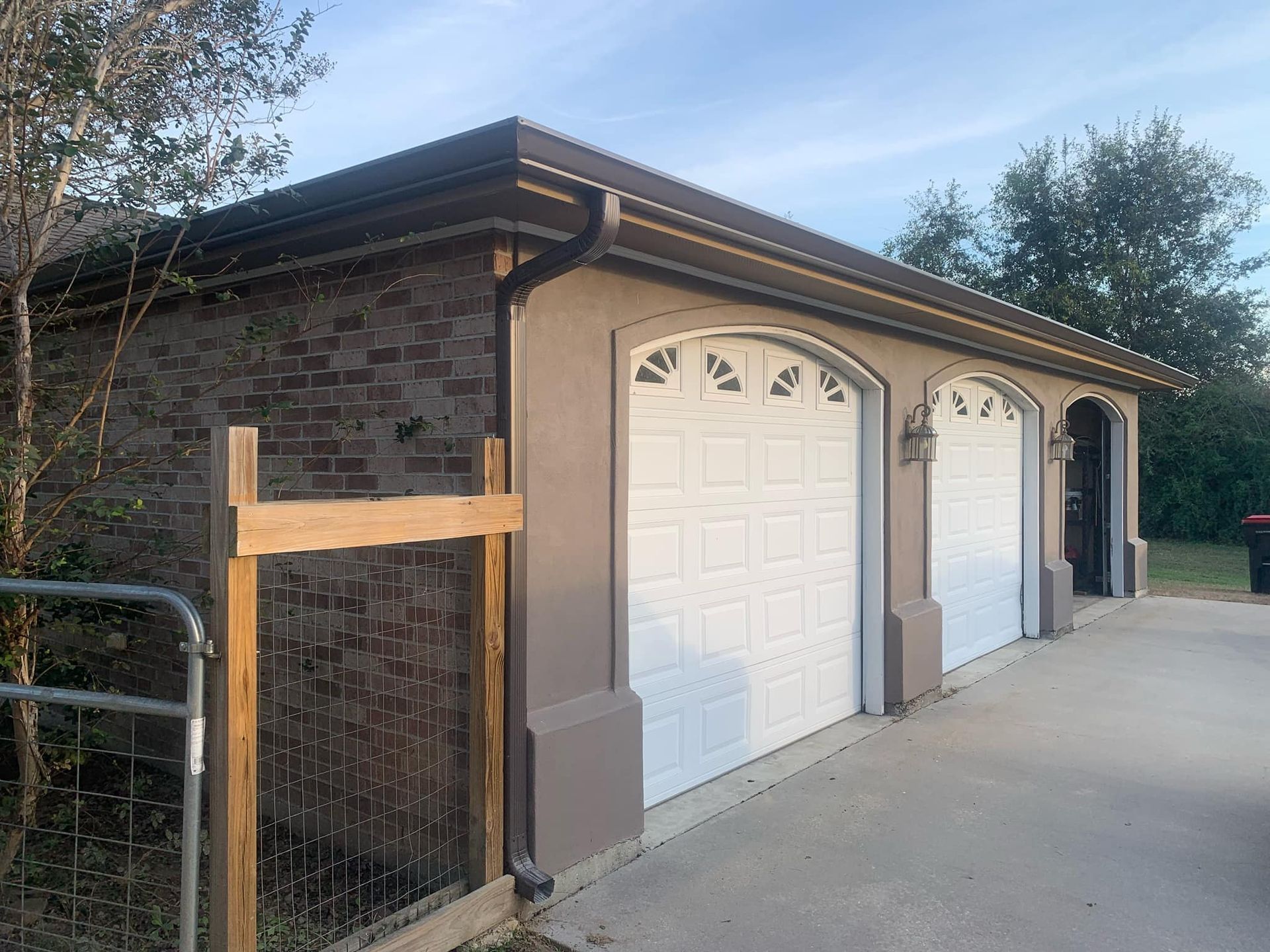 A garage with three white garage doors and a wooden fence.
