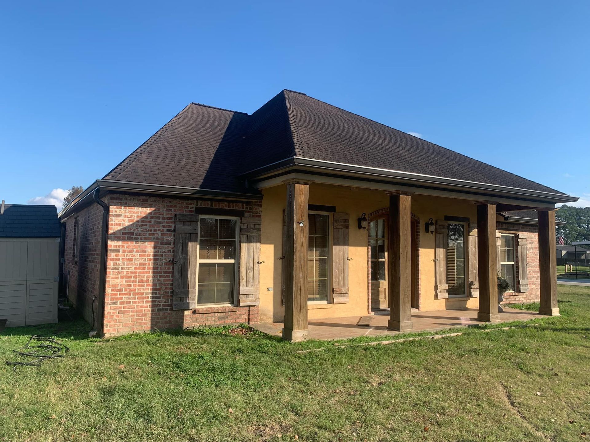 A small brick house with a porch and a garage in the backyard.