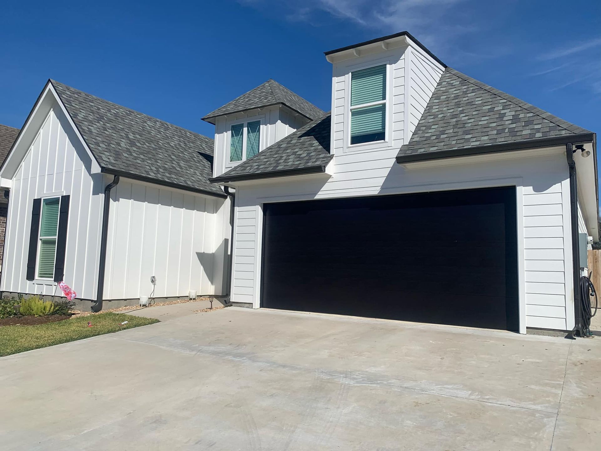 A white house with a black garage door and a gray roof