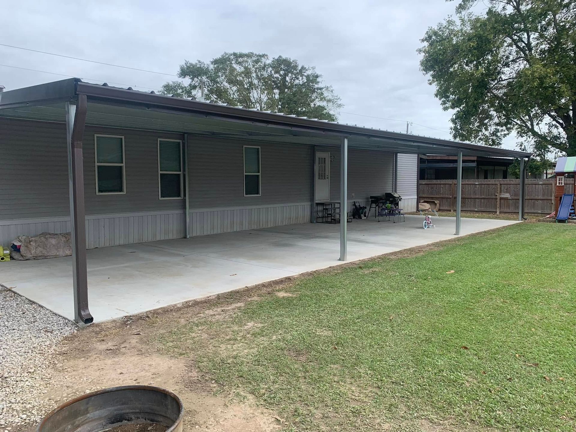 A mobile home with a covered porch and a fire pit in front of it.