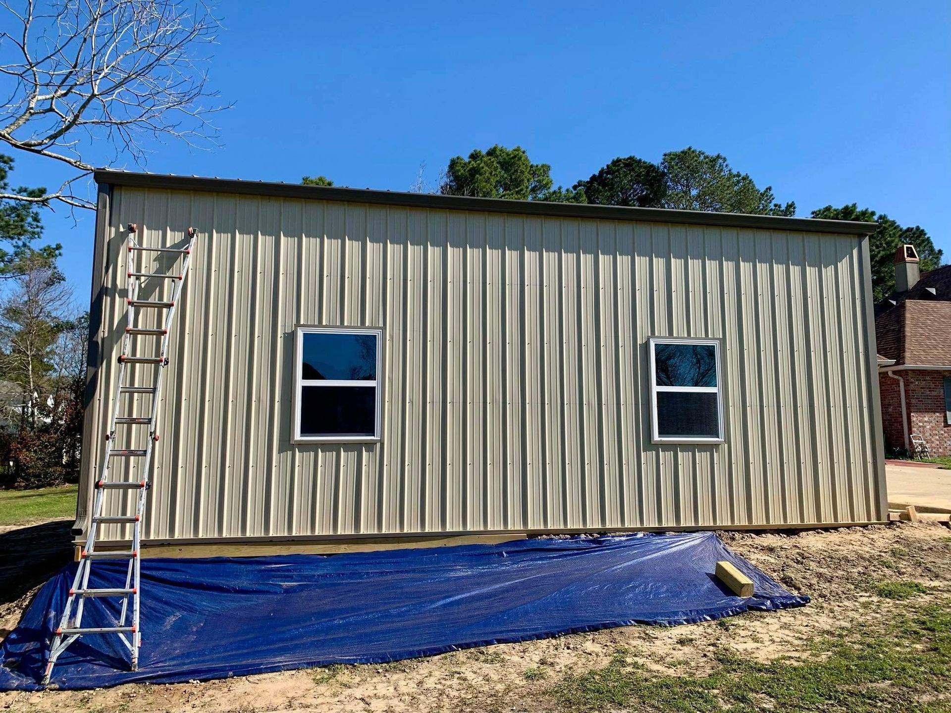 A metal building with a ladder on the side of it is being painted.