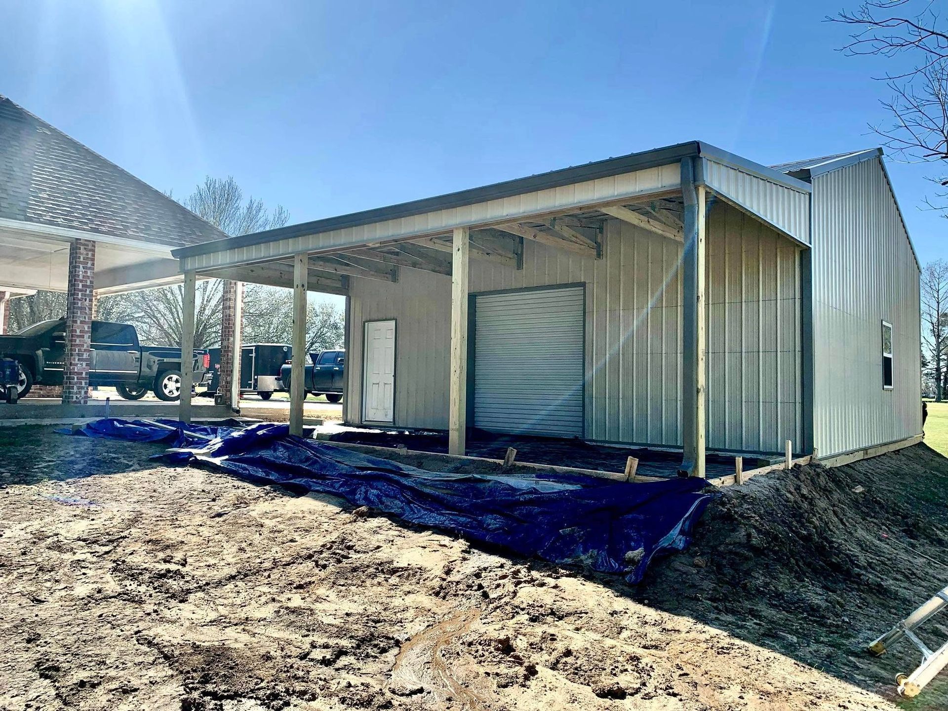 A large metal building is being built next to a dirt field.