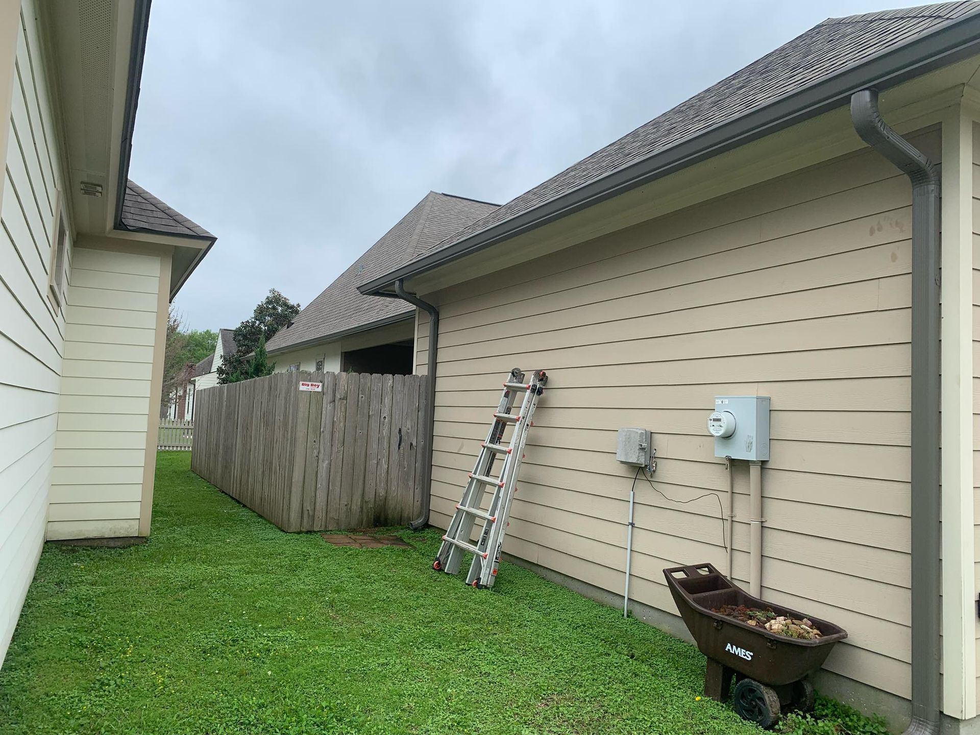 A ladder is sitting on the side of a house next to a wheelbarrow.
