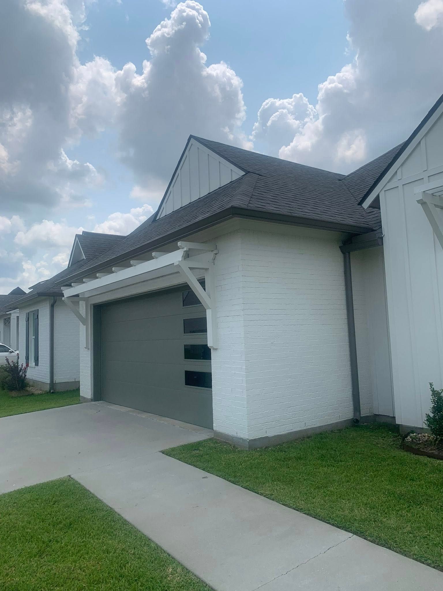 Suburban house with white siding, gray roof, driveway, and sidewalk under a cloudy sky