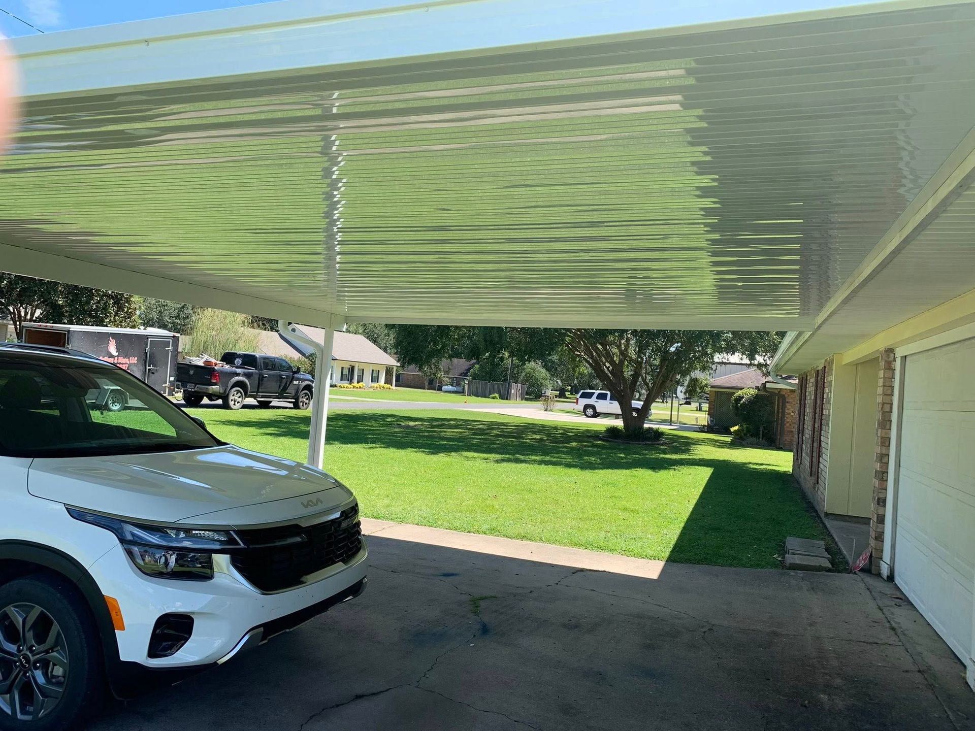 White SUV parked under a striped carport beside a garage, with a green lawn in the background.
