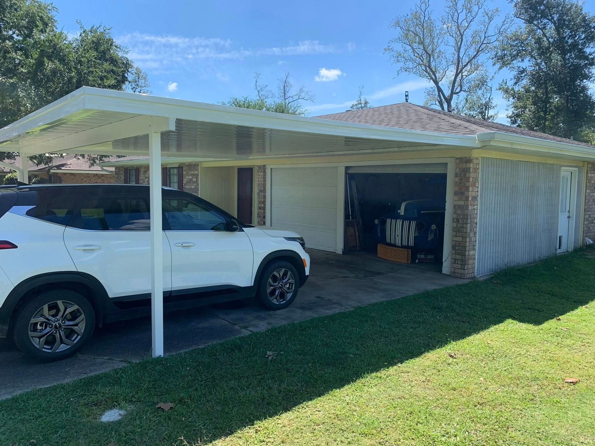 White SUV parked under a carport beside a brick house on a sunny day