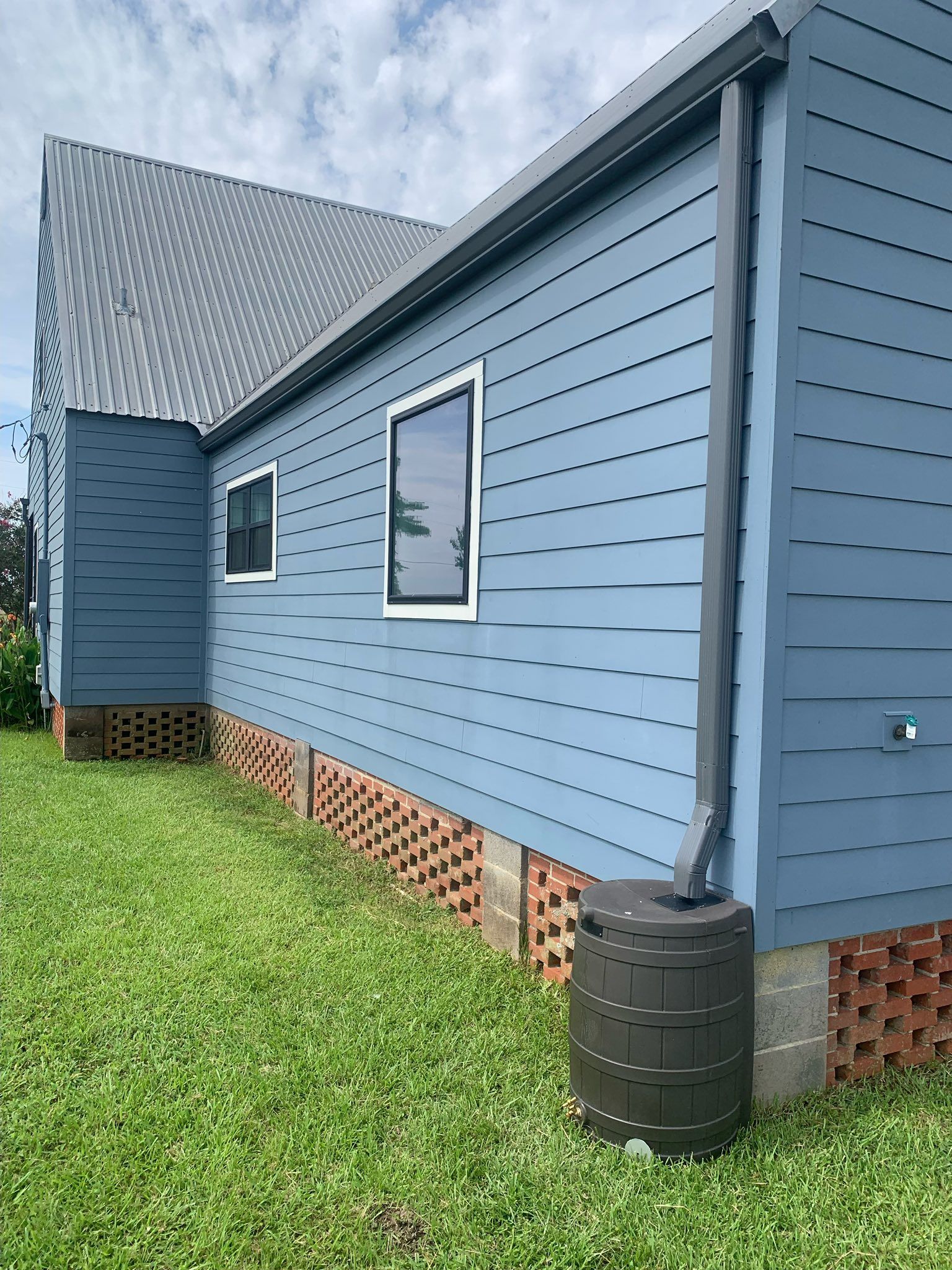 Blue house exterior with gray roof, small windows, and rain barrel beside the wall.