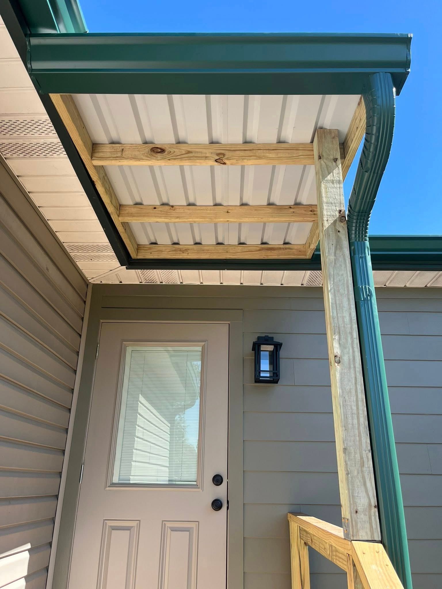 Front porch with a beige door, wall light, and a teal roof overhang with wood supports