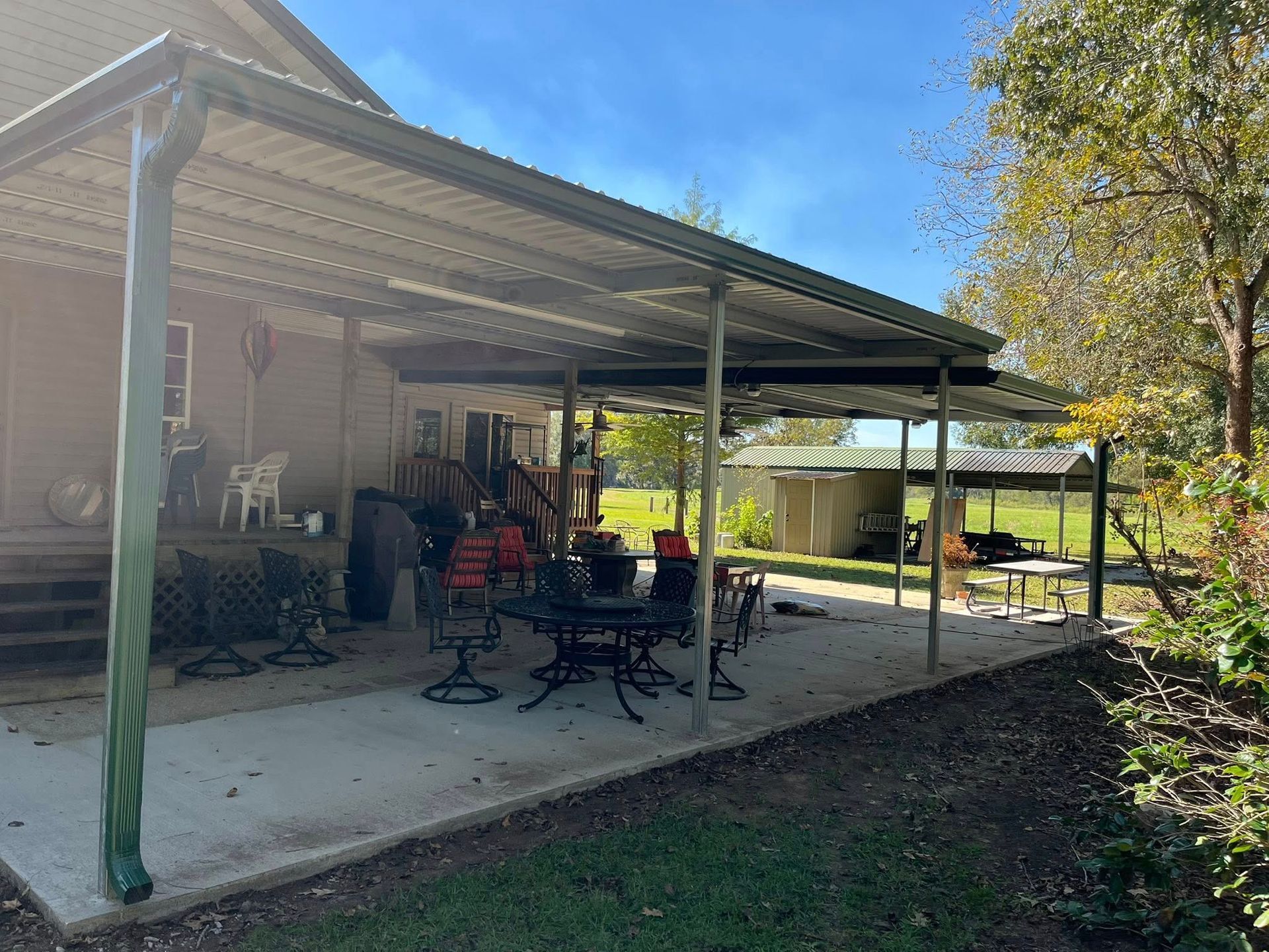 Covered patio with outdoor furniture beside a house, overlooking a sunny backyard