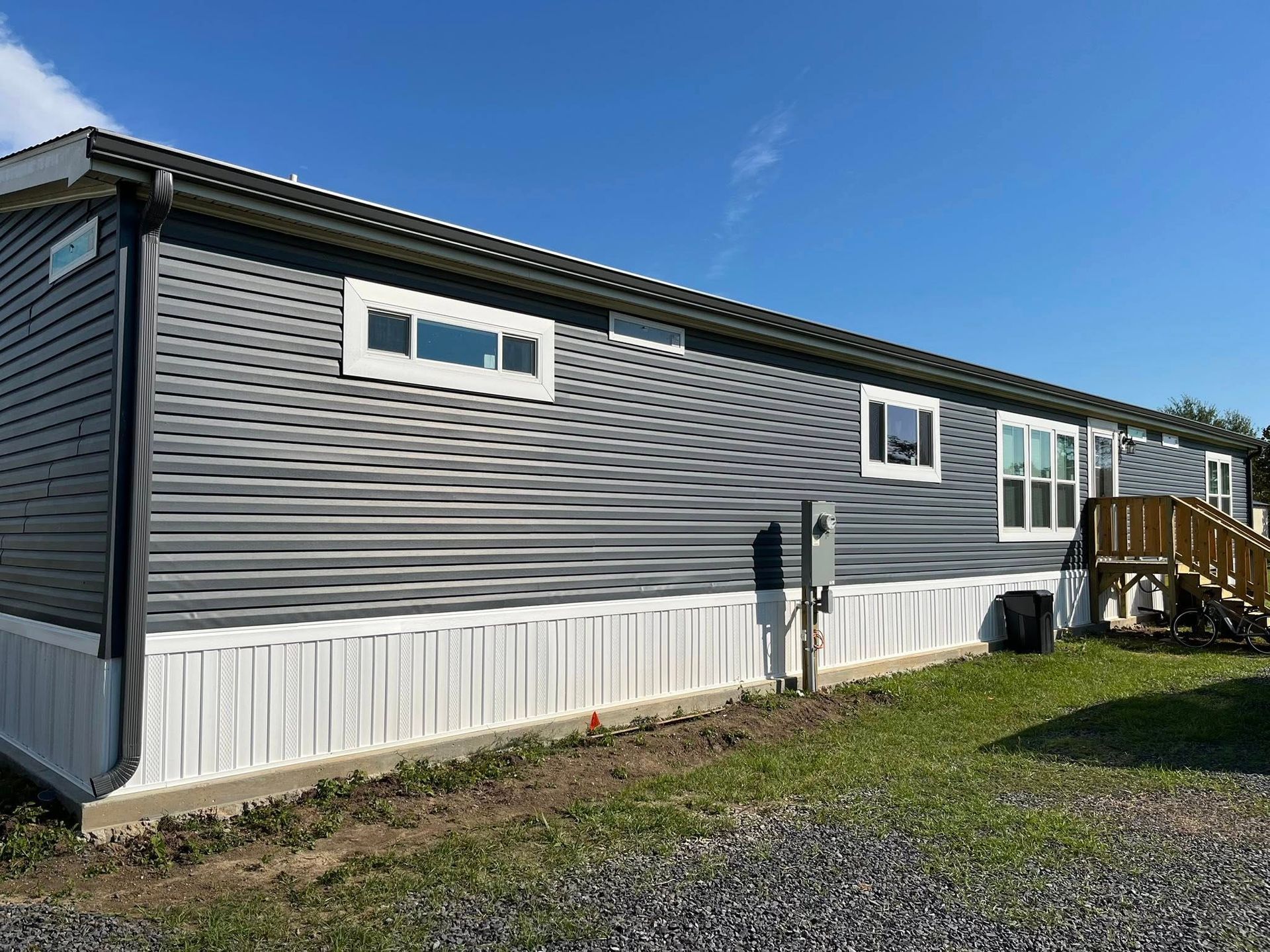 Gray mobile home with white trim and small porch on a grassy lot under a blue sky