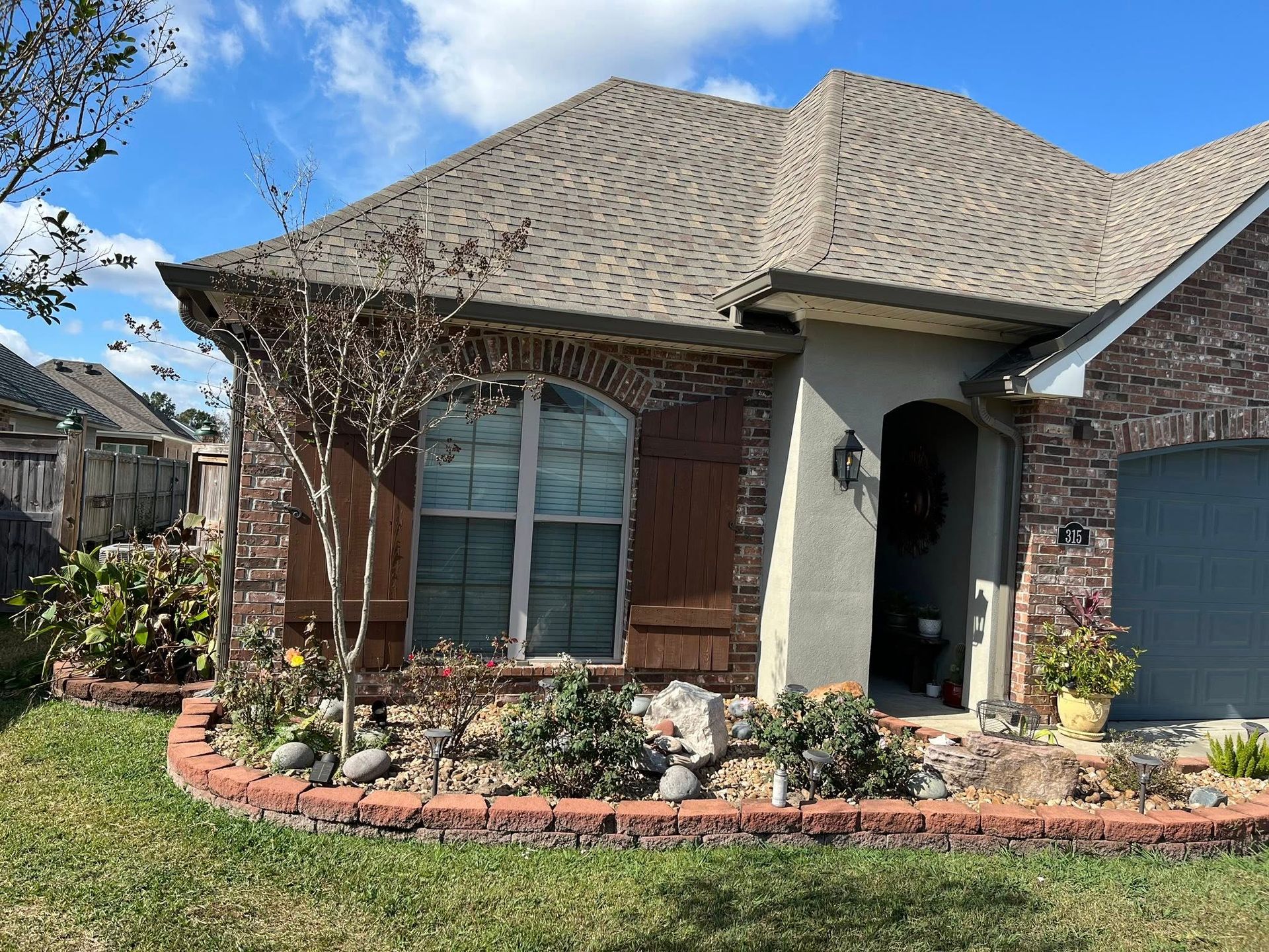 Front view of a brick house with a gray roof, blue garage door, and landscaped flower bed