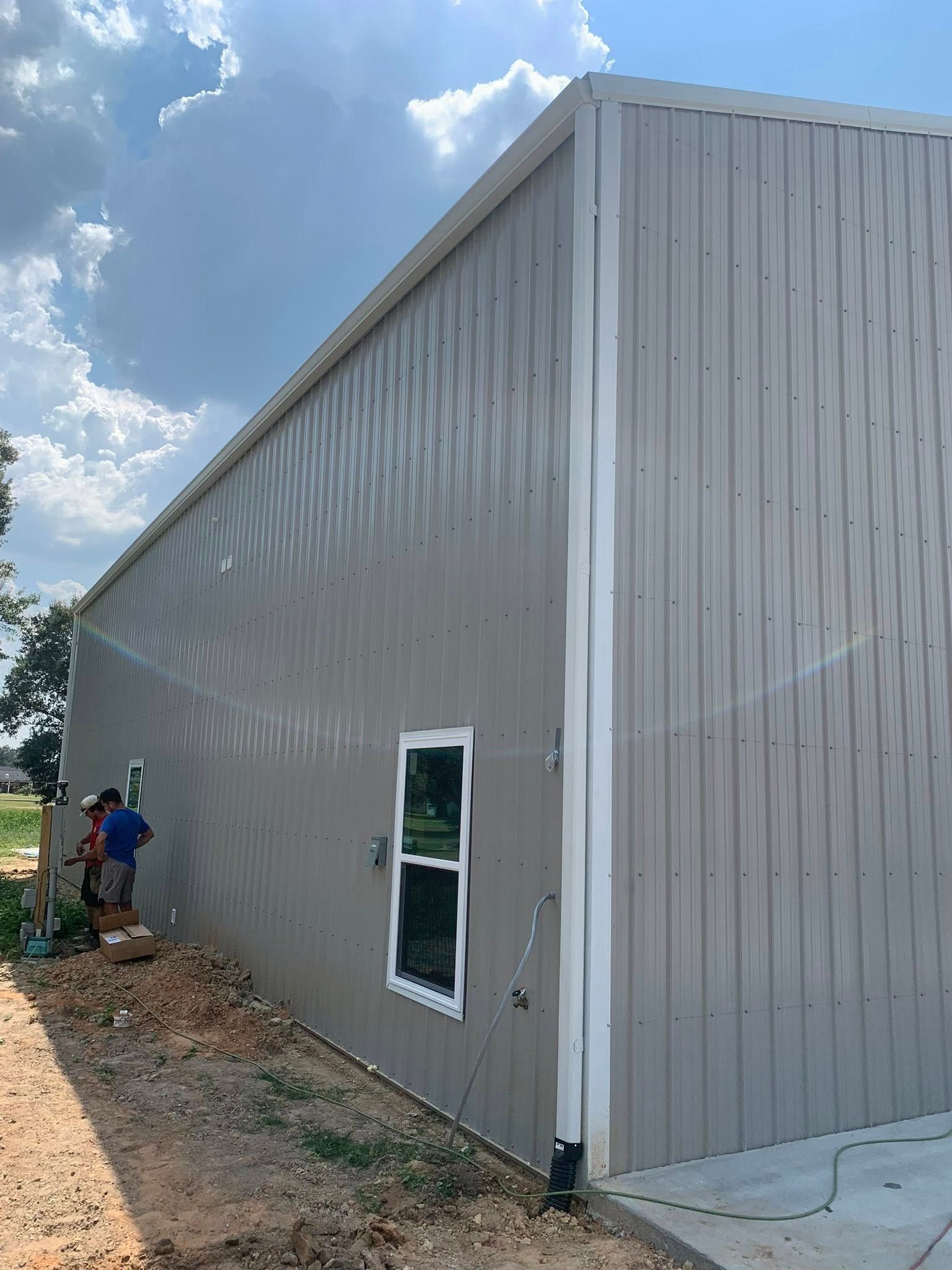 White metal warehouse exterior with a small window and a worker near the left side.