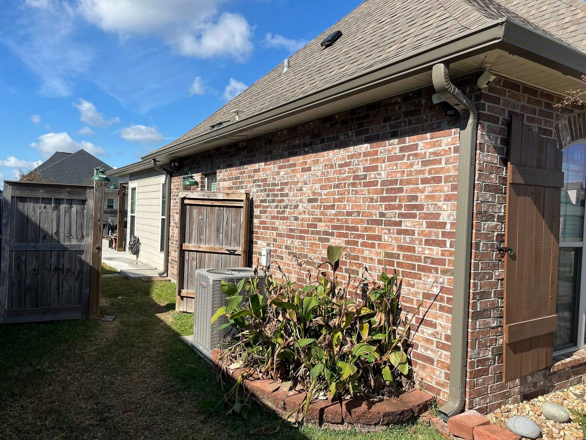 Brick house side yard with wooden gate, garden bed, and blue sky