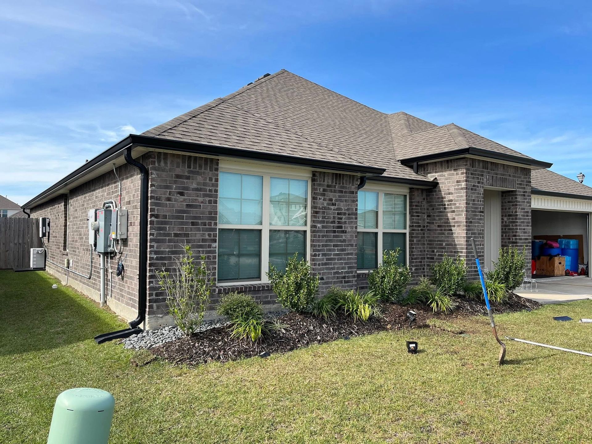 Brick suburban house exterior with gray roof, front windows, and a lawn under construction