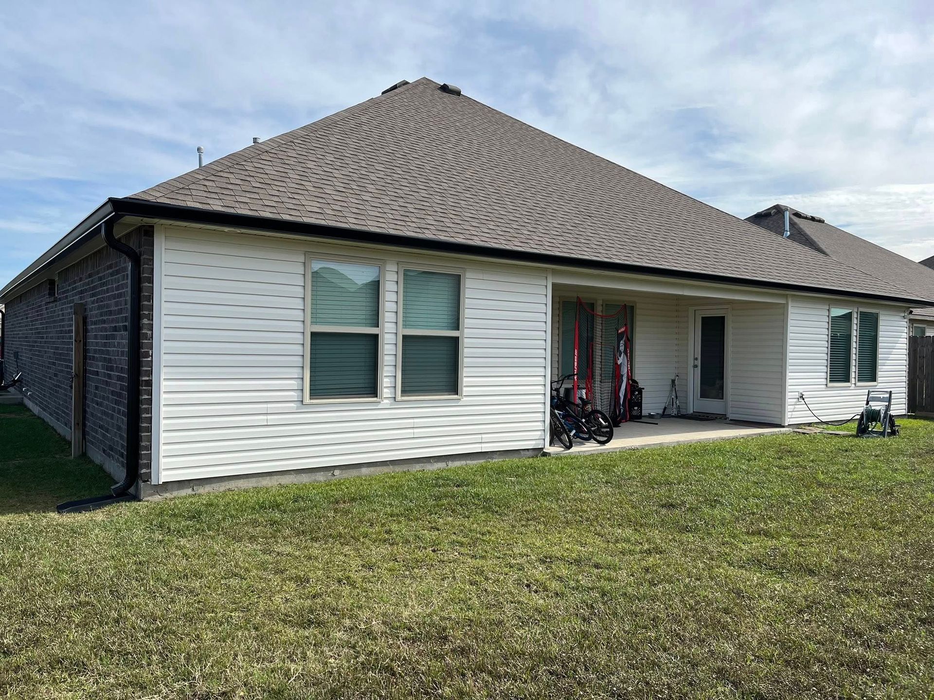 Single-story white house with gray roof, front porch, bikes, and a grassy yard under a cloudy sky