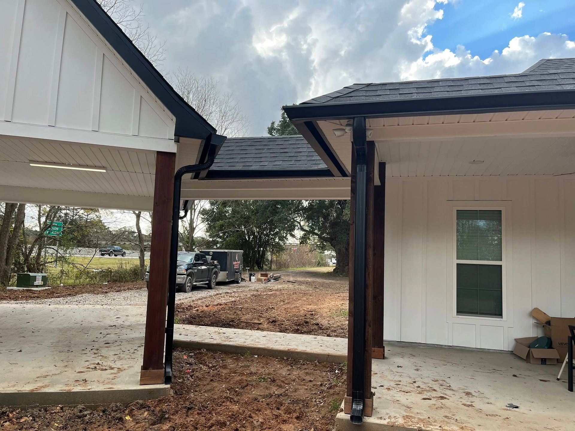 Covered walkway connecting two white buildings on a concrete patio, with brown posts and trees in the background.