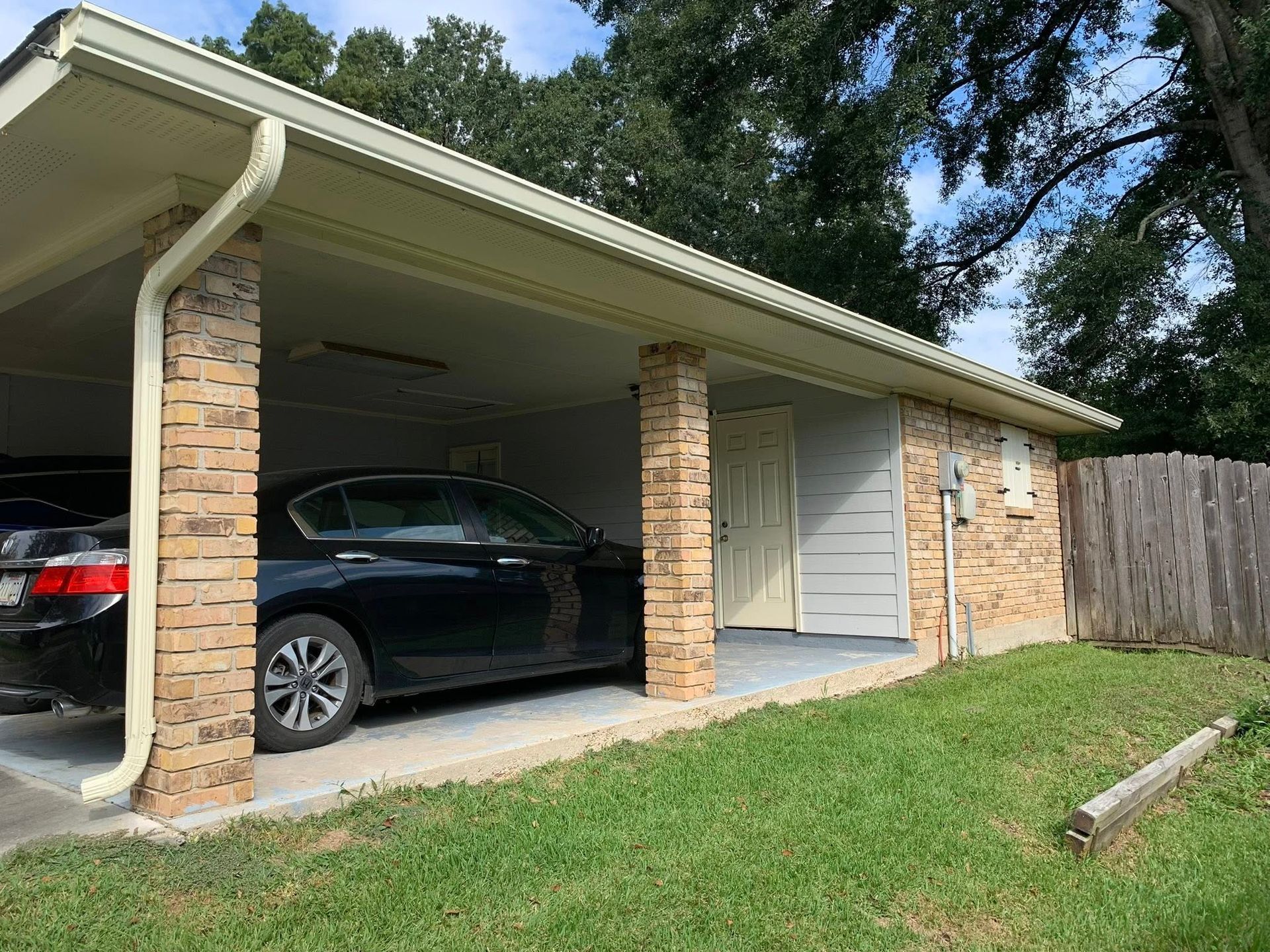 Carport attached to a brick house with two parked cars and a grassy yard.
