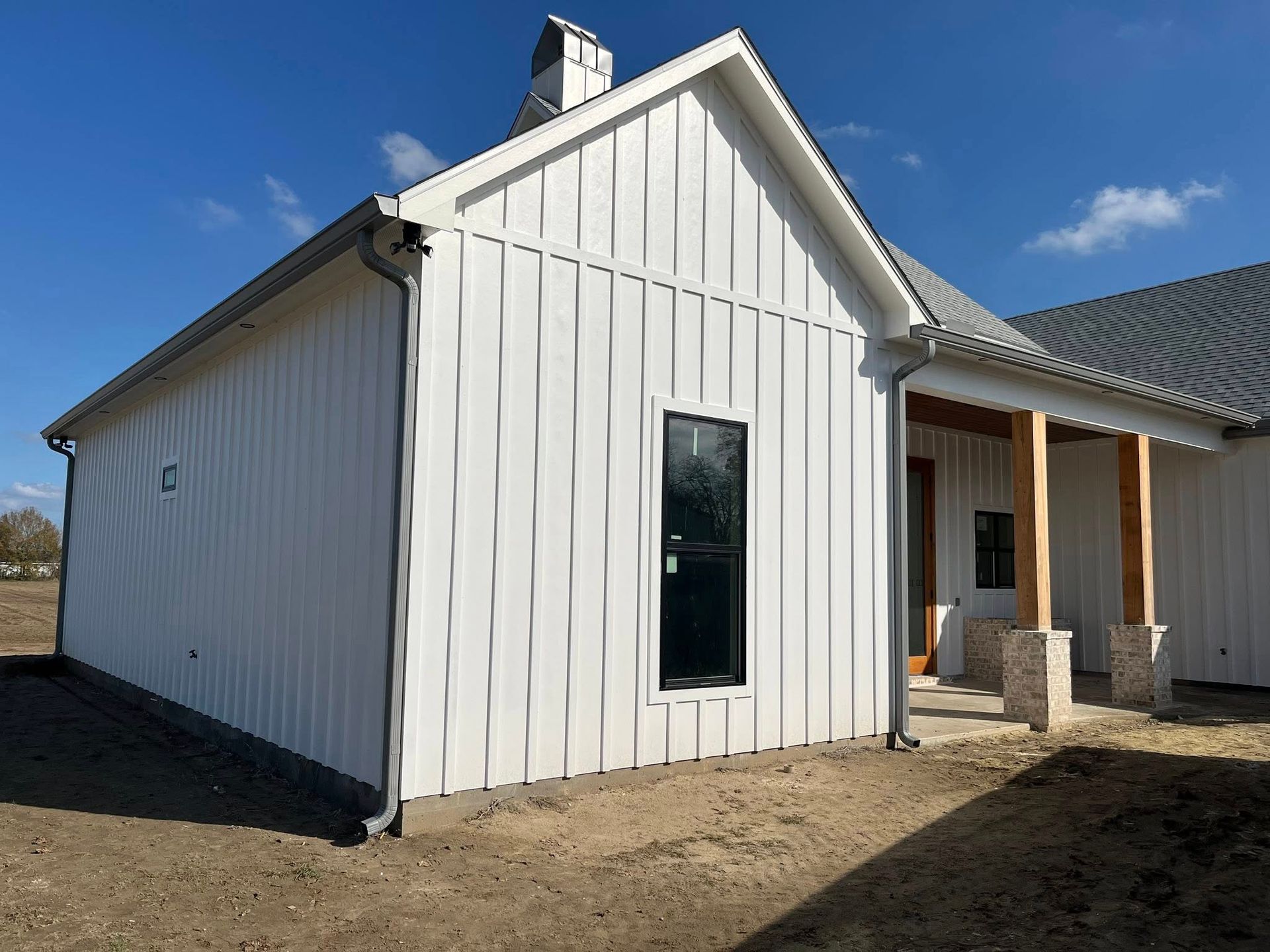 White gabled house exterior with vertical siding, a tall narrow window, and a covered porch under blue sky