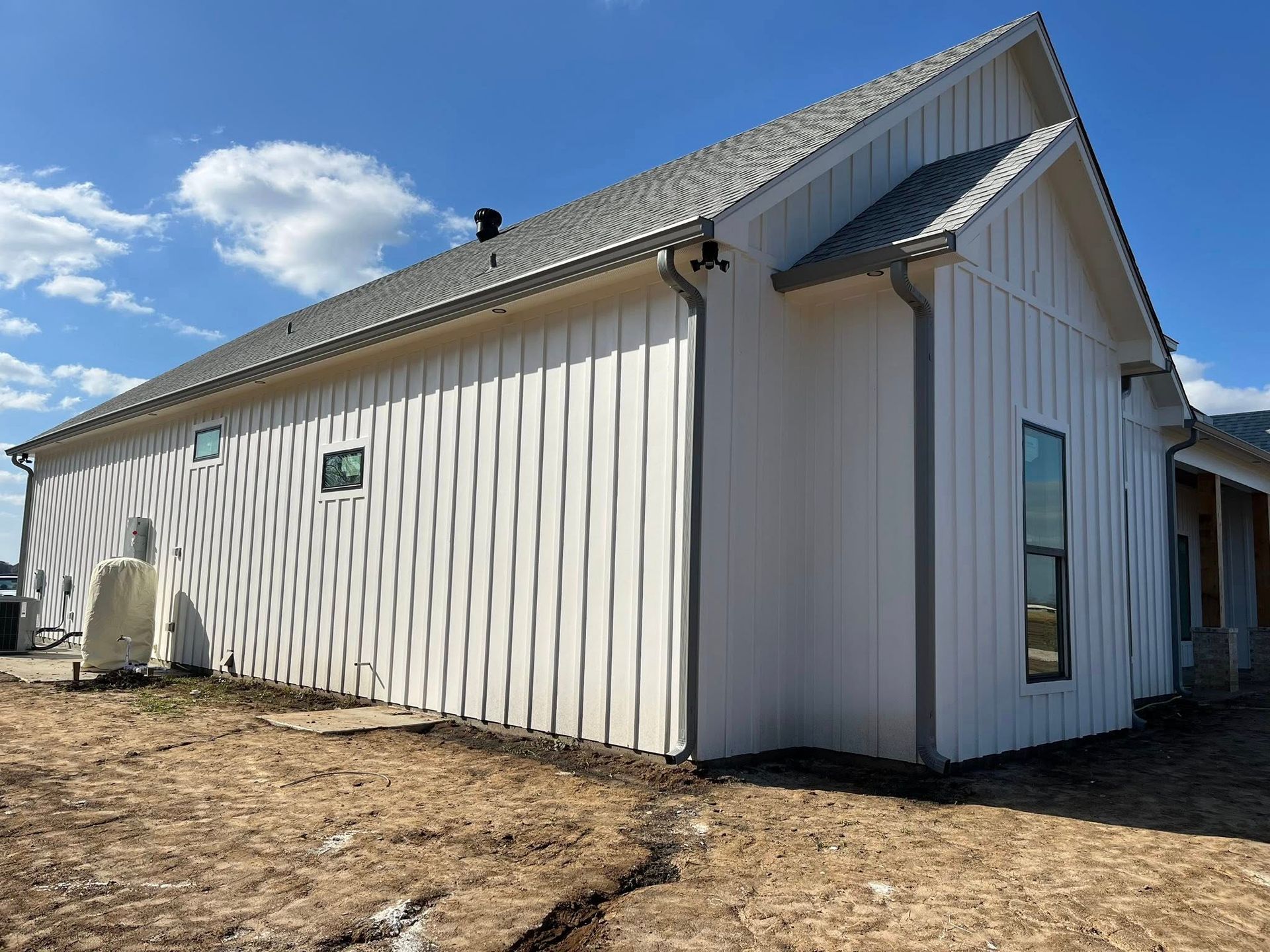 White-sided rural building with gray roof and small windows under a blue sky