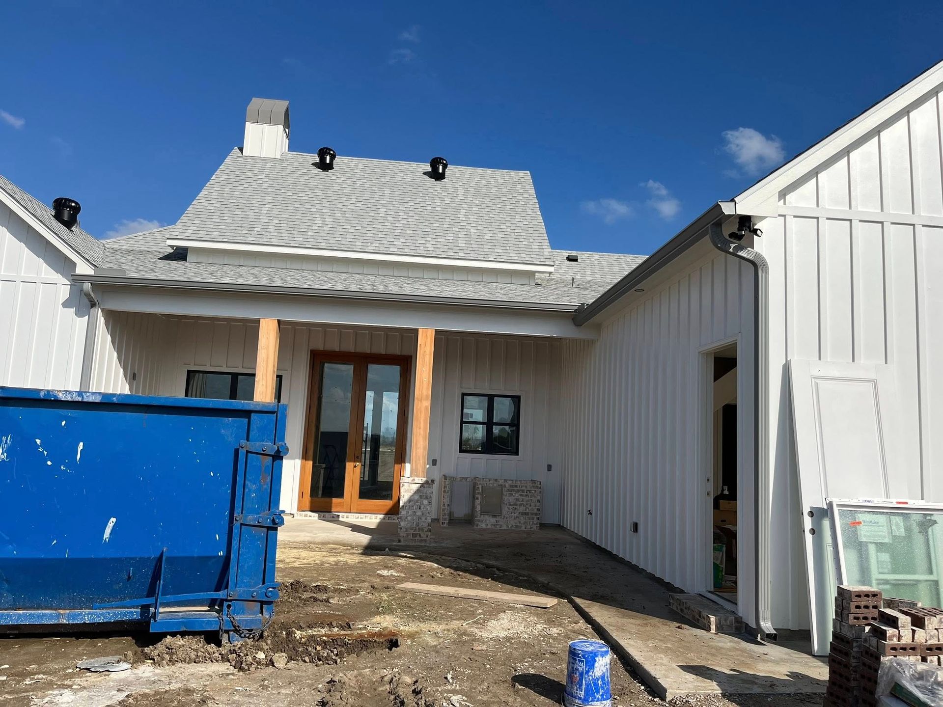 Backyard view of a house under construction with a blue dumpster and unfinished siding