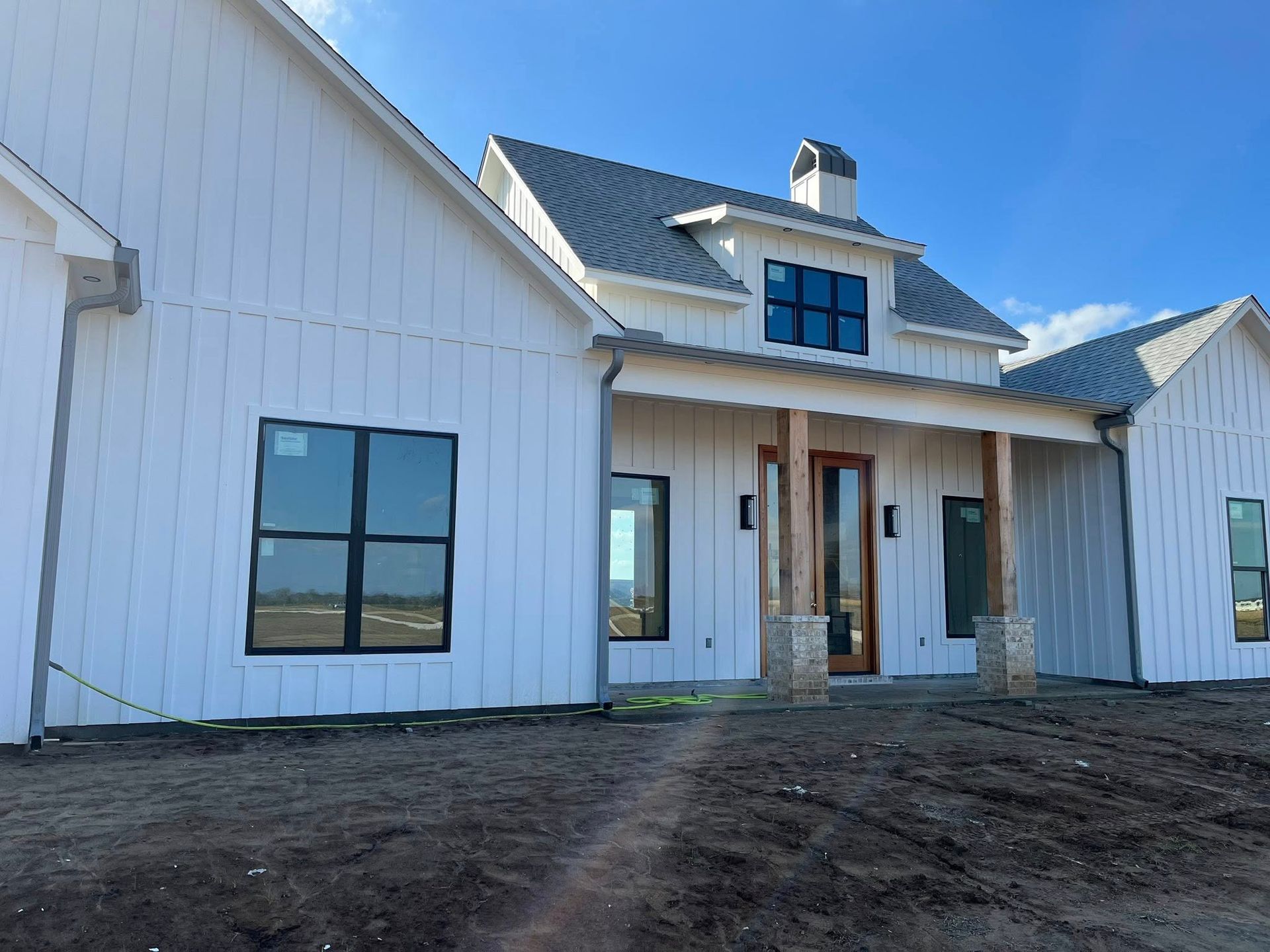 Modern white house exterior with black-trimmed windows and a covered front porch under a blue sky