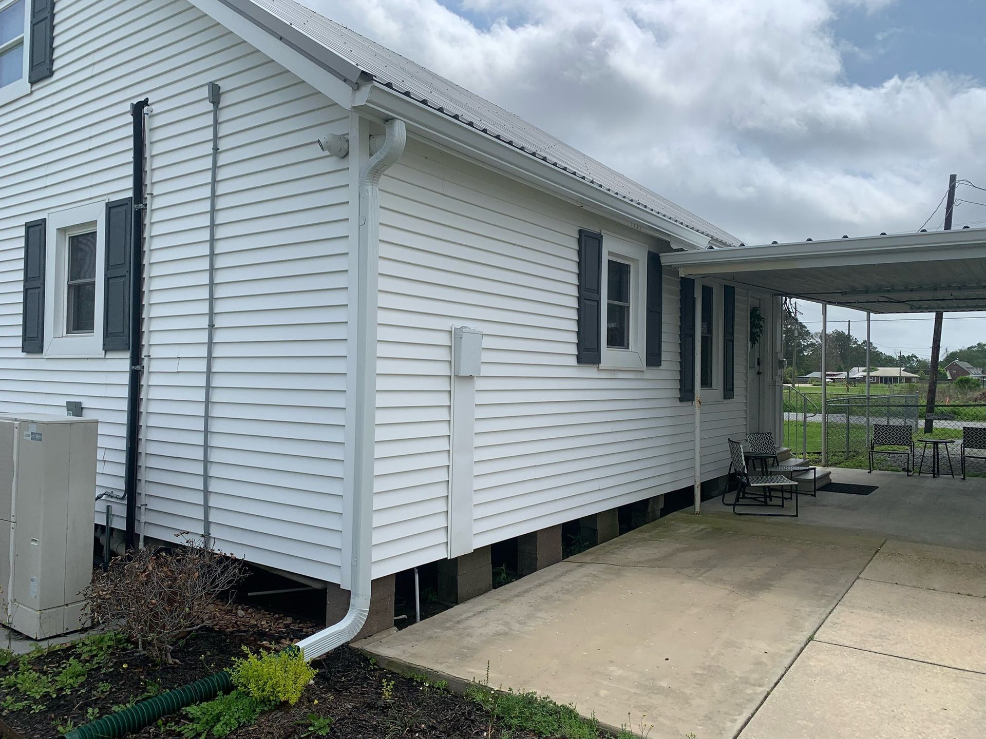 White vinyl house exterior with windows, white downspout, and a concrete patio beside a covered carport.