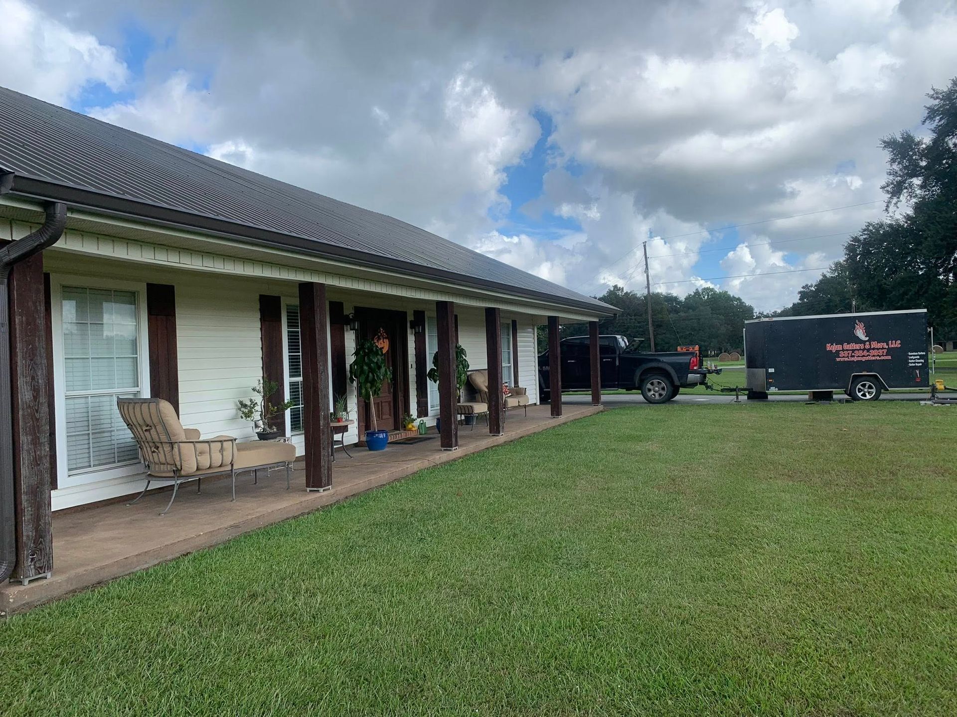 Rural house with a covered porch, green lawn, and a black truck with trailer parked nearby