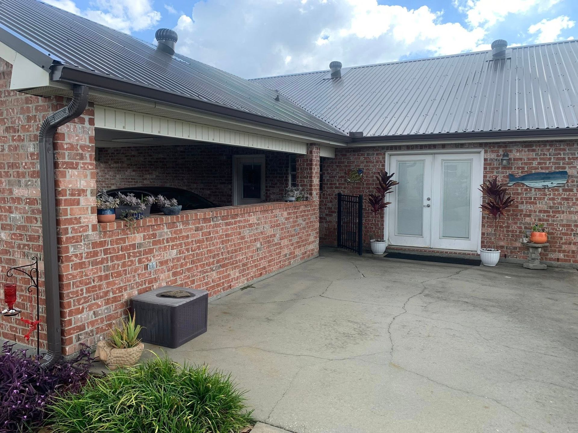 Brick courtyard with covered seating area, white double doors, and gray roof on a cloudy day