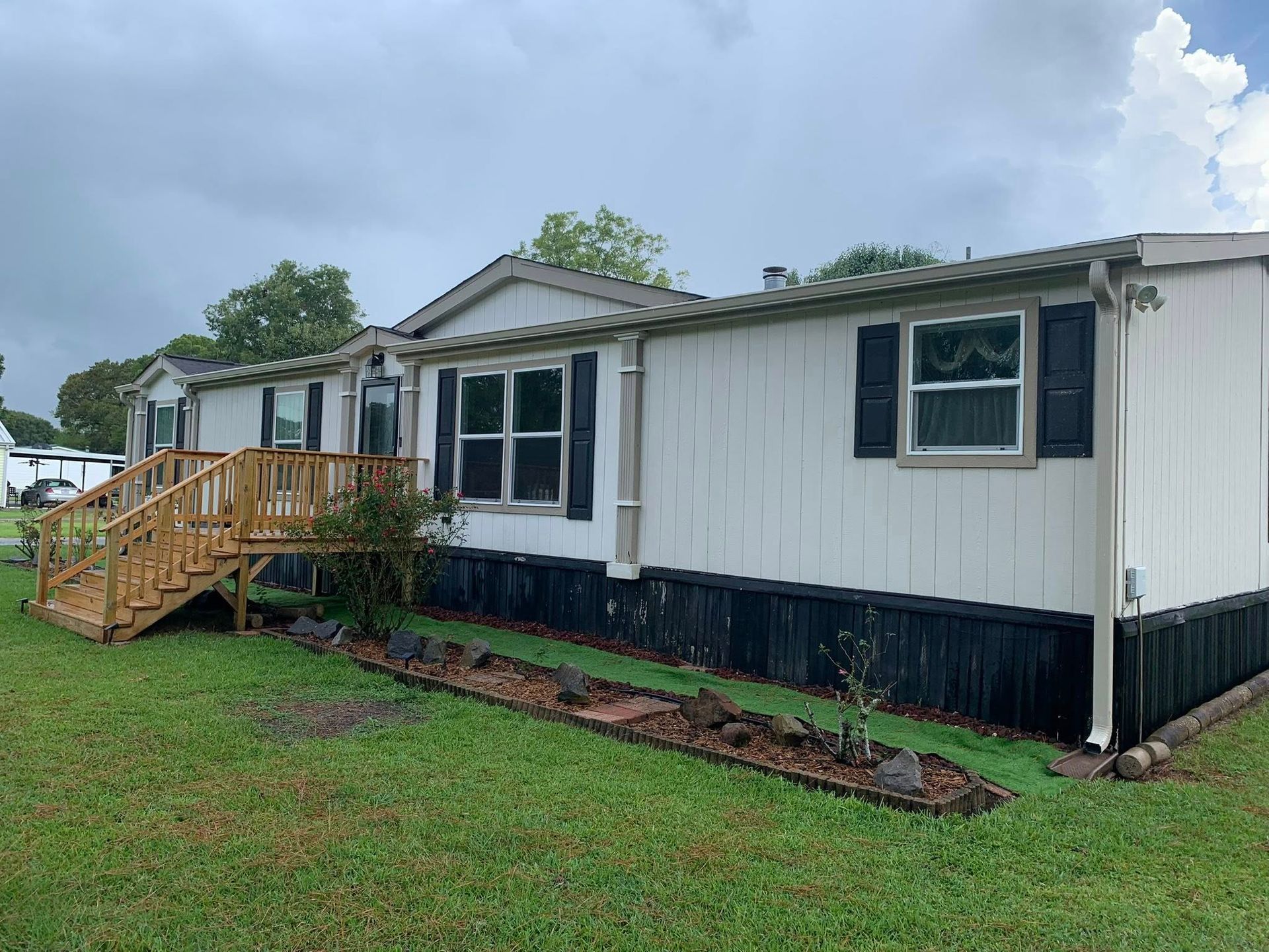 White mobile home with wooden steps on a grassy lot under a cloudy sky