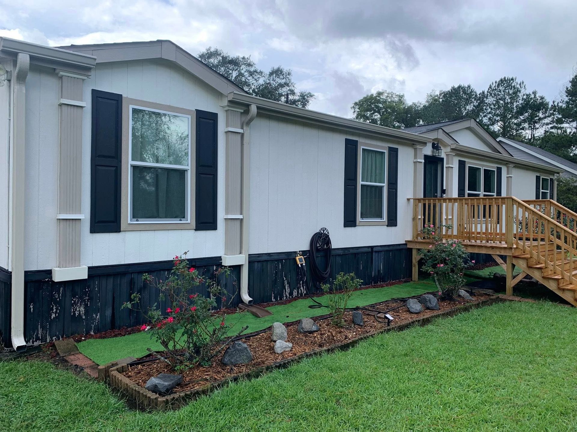 Manufactured home with new wooden front steps and landscaped flower bed on a green lawn