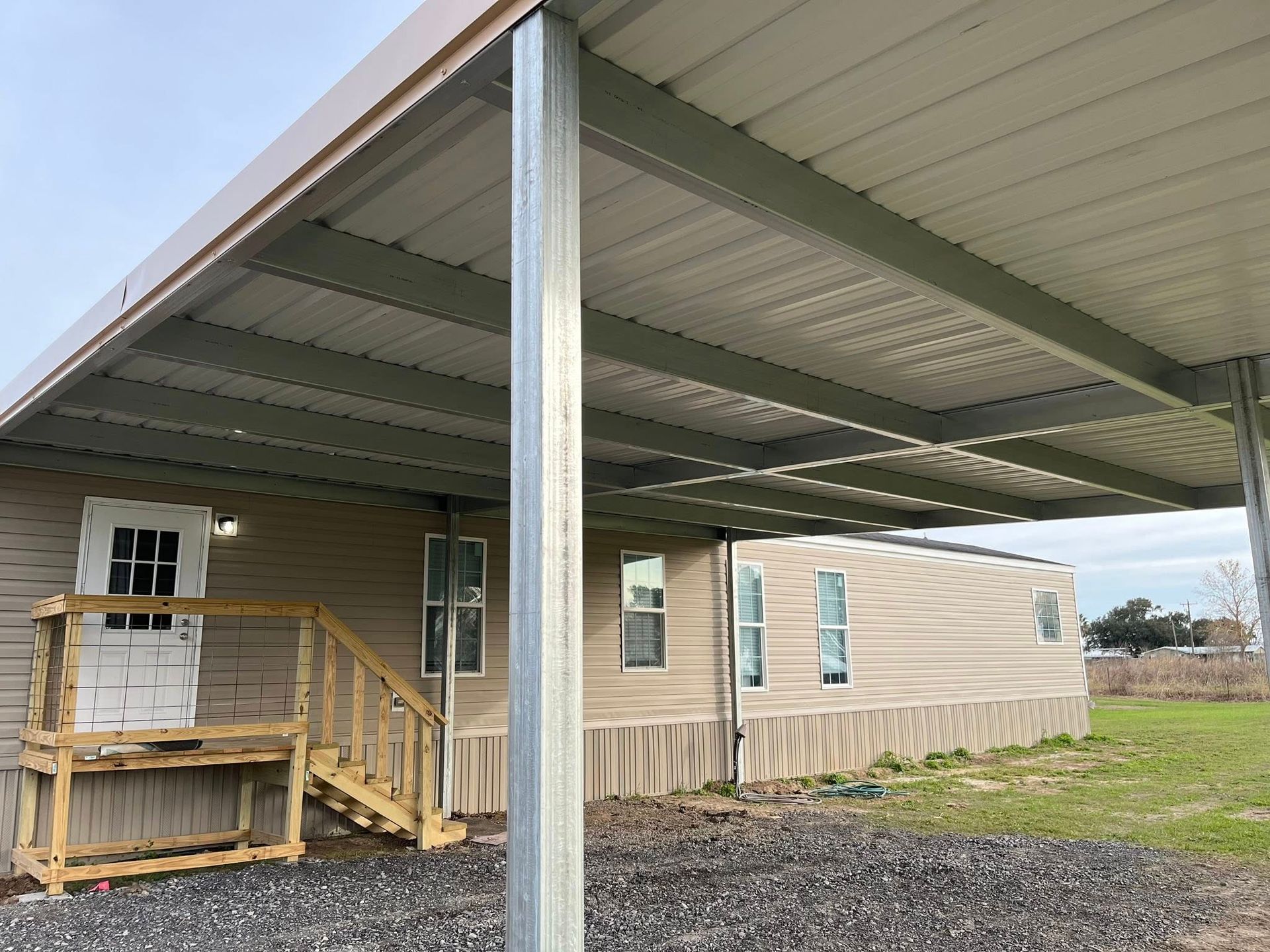 Covered porch and metal carport beside a beige house in a rural yard