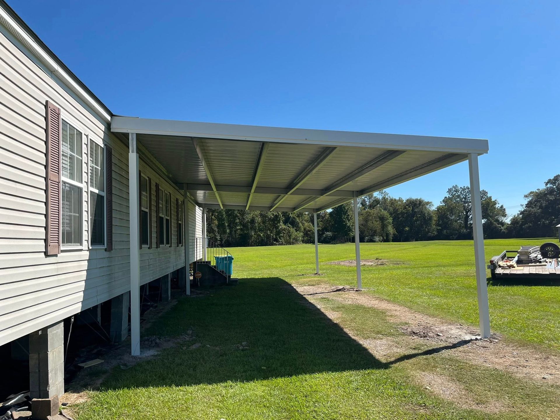 Mobile home with covered carport beside a grassy yard under a clear blue sky
