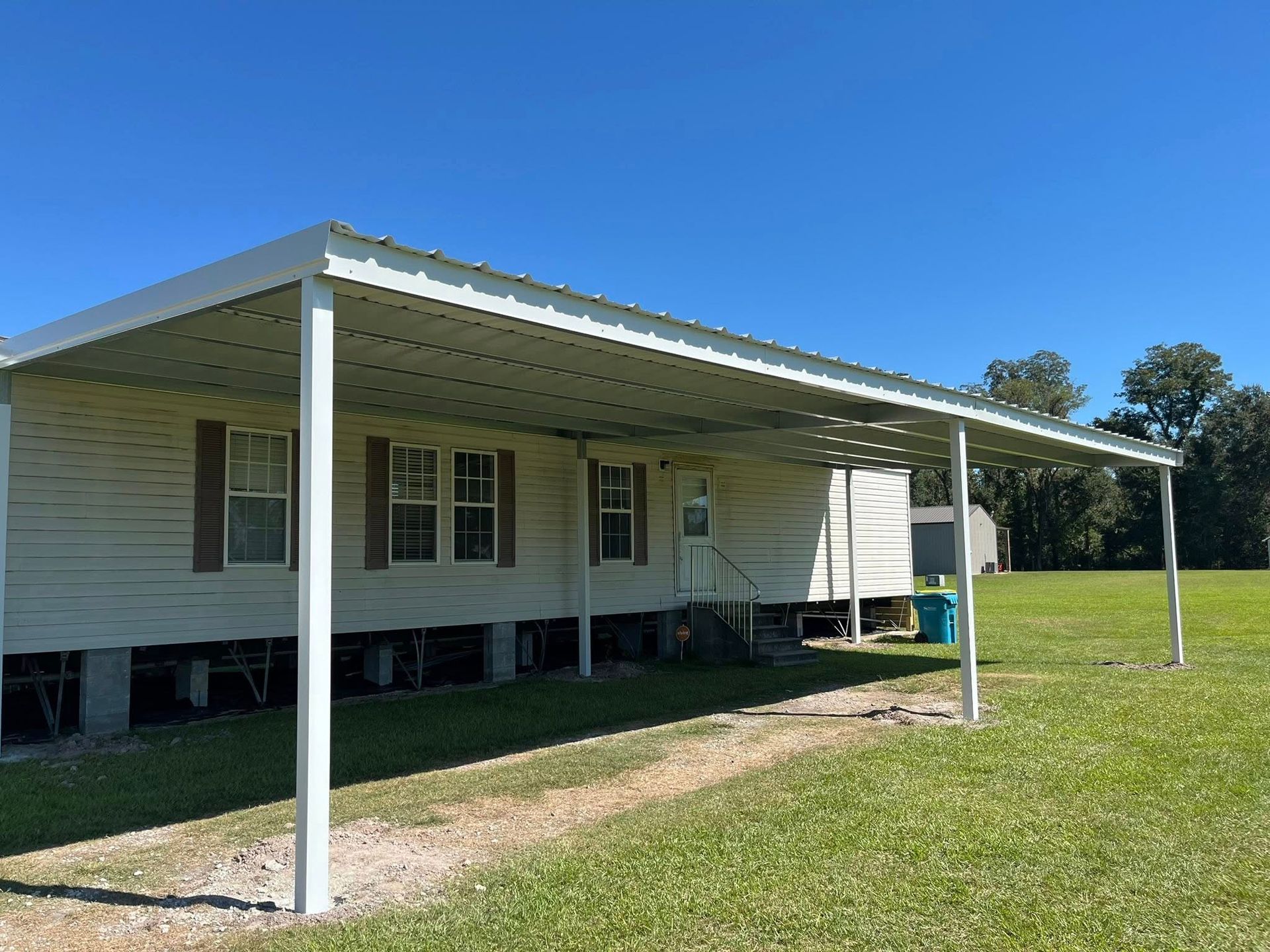 White rural house with a covered porch and metal awning on a grassy lawn under a blue sky