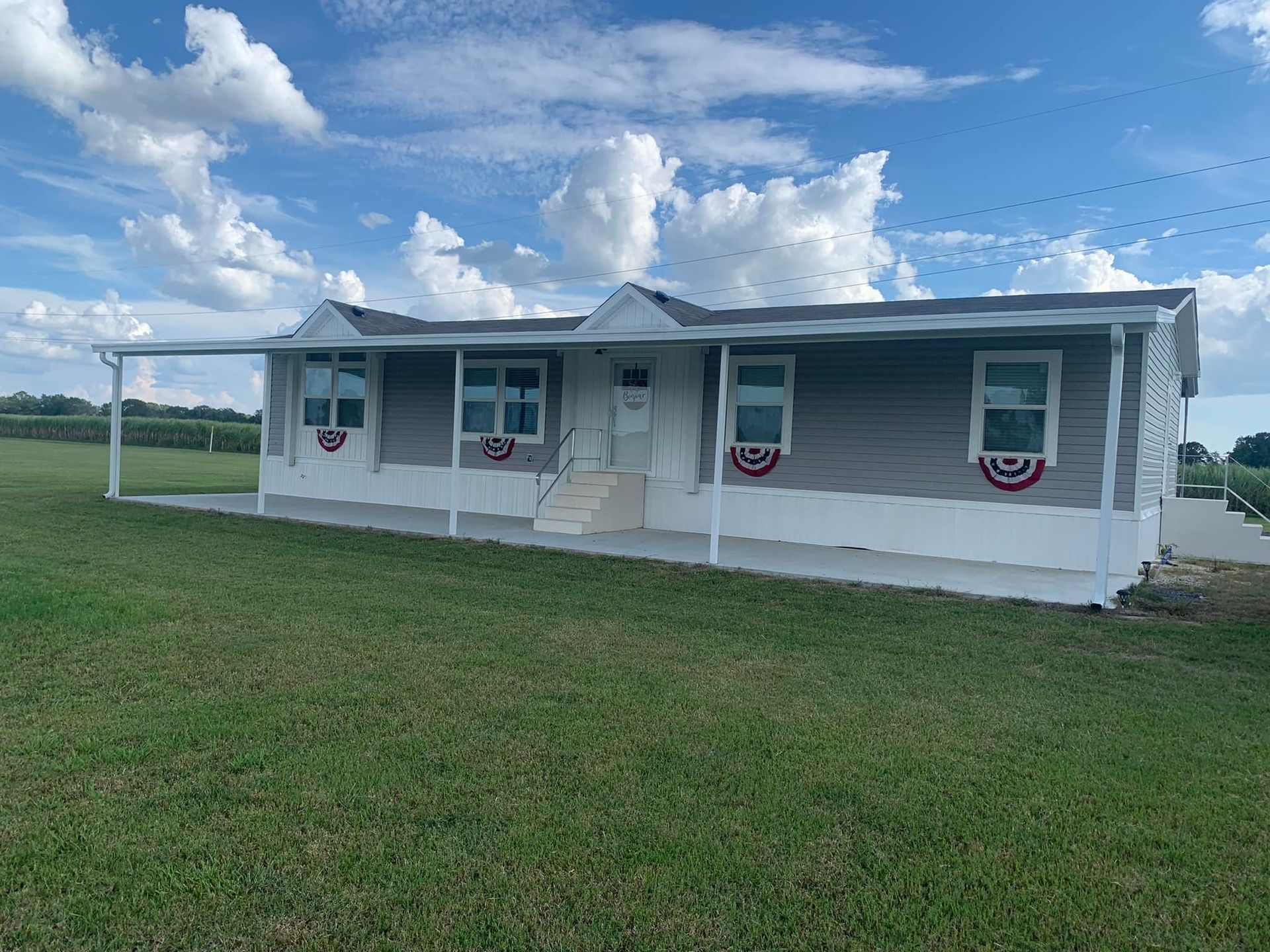 White mobile home with red-white-blue bunting on a grassy field under a cloudy blue sky