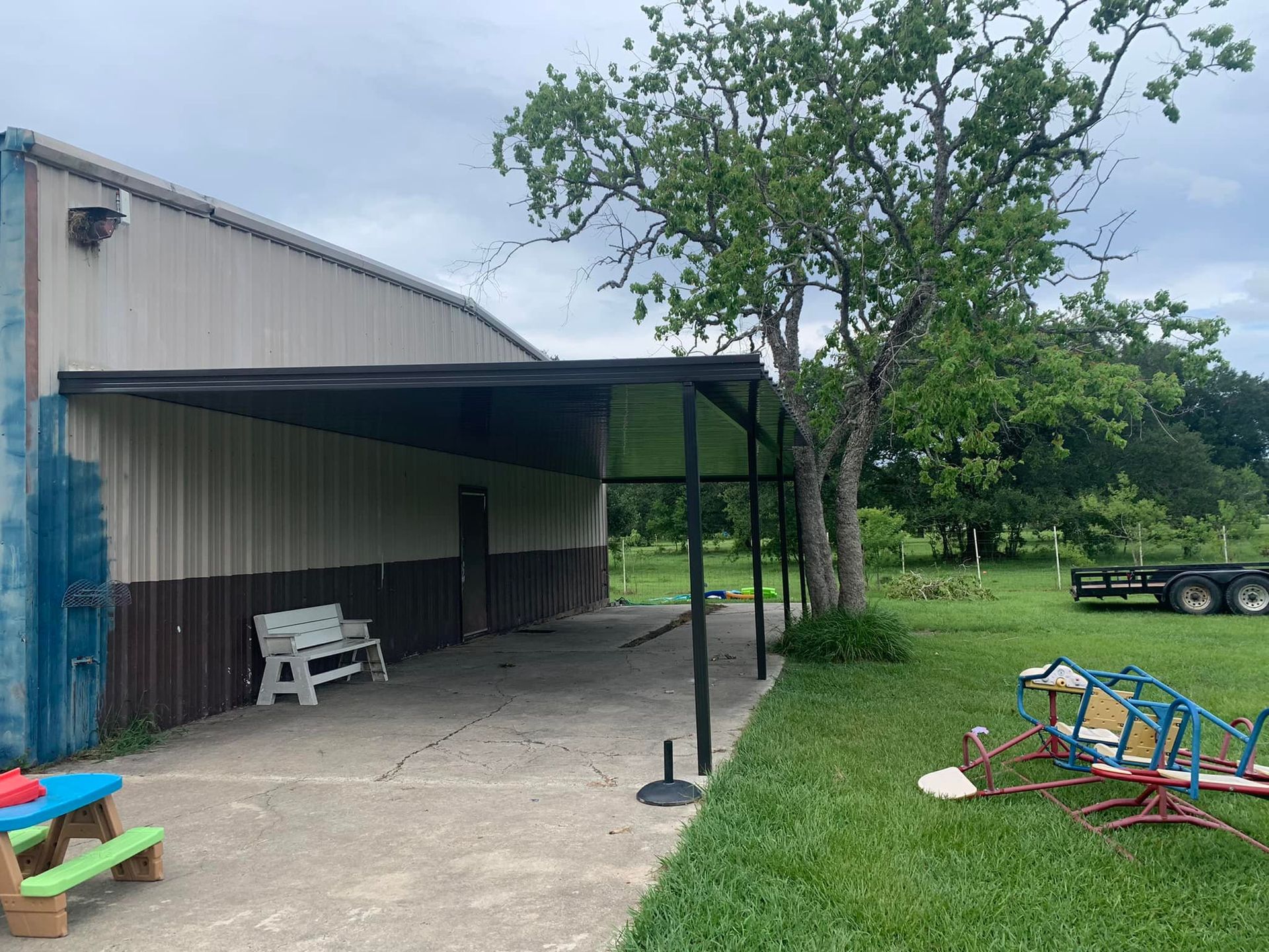 Backyard patio beside a shed, with a tree, lawn, and children’s play equipment