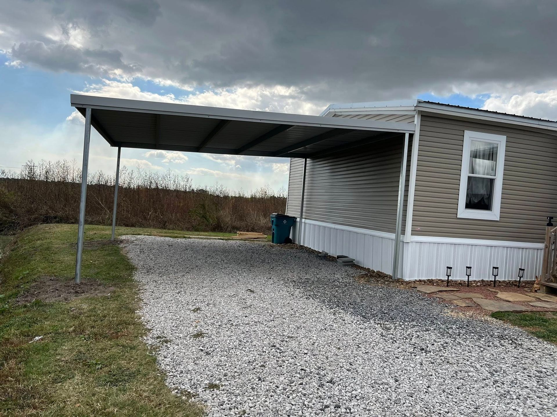 Mobile home with a gravel driveway and covered carport in a rural setting