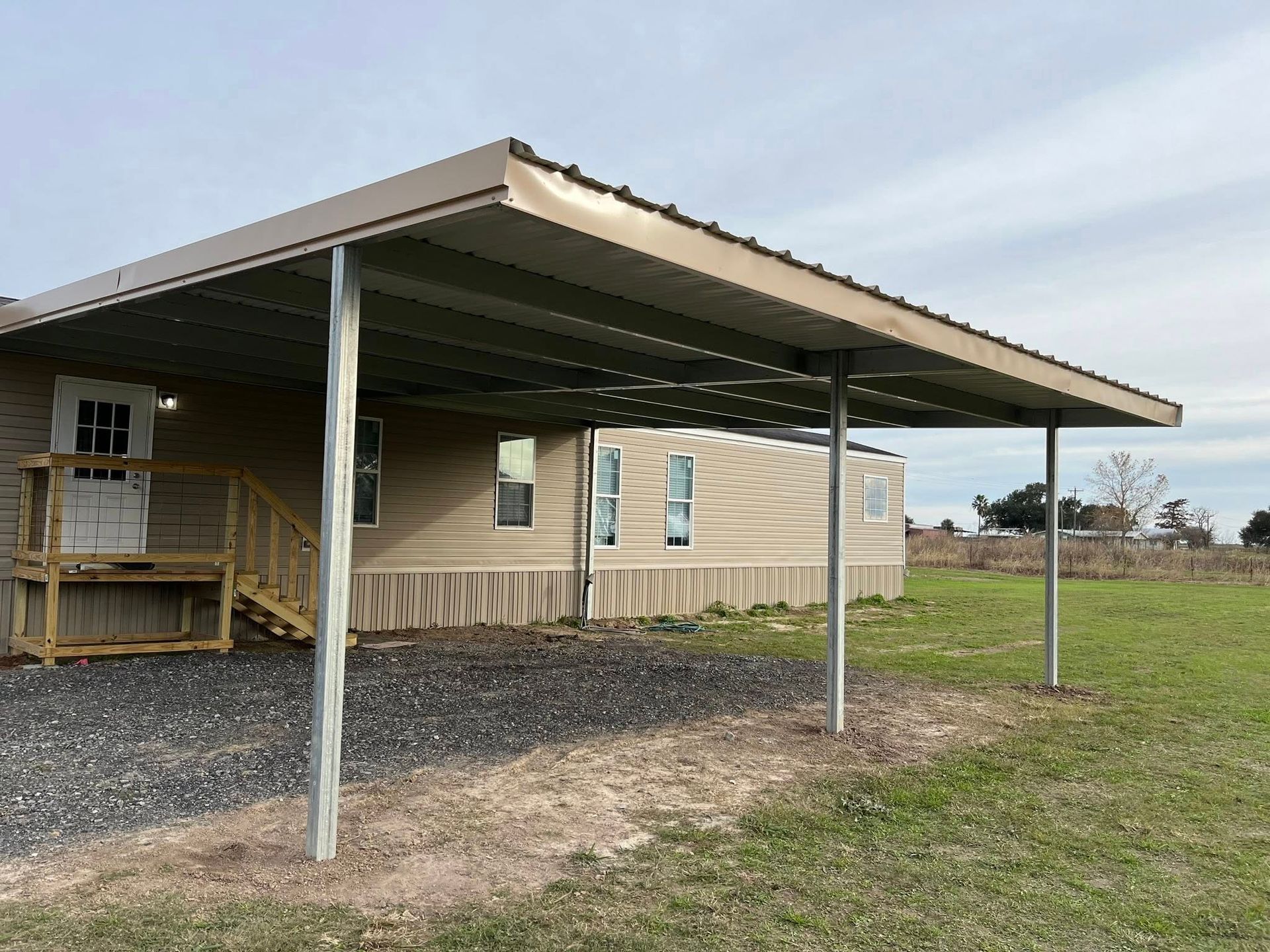 Covered porch and carport attached to a beige house in a grassy rural yard.