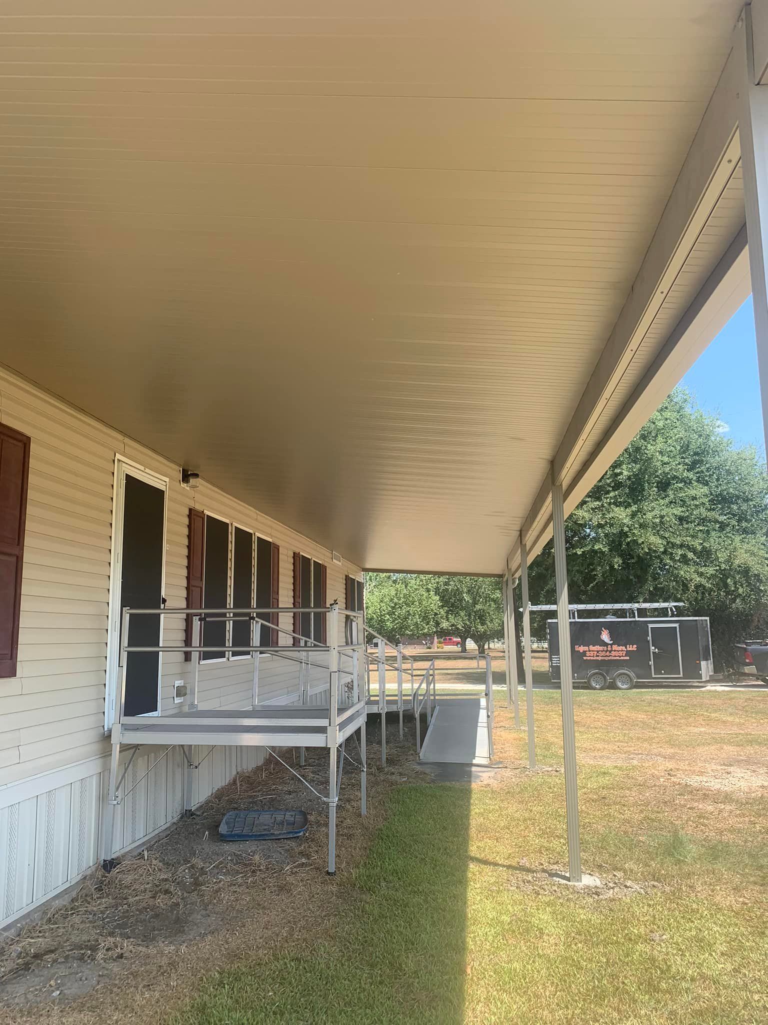Covered porch along the side of a beige house with white railings and a grassy yard.